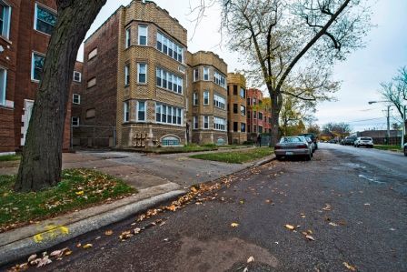 Apartment buildings on a street; a parked car, and a tree are in the foreground. Overcast sky.