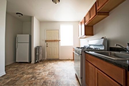 Kitchen with light brown cabinets, stove, sink, refrigerator, and door with window.