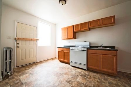 Kitchen with light brown cabinets, white stove, window, and door.
