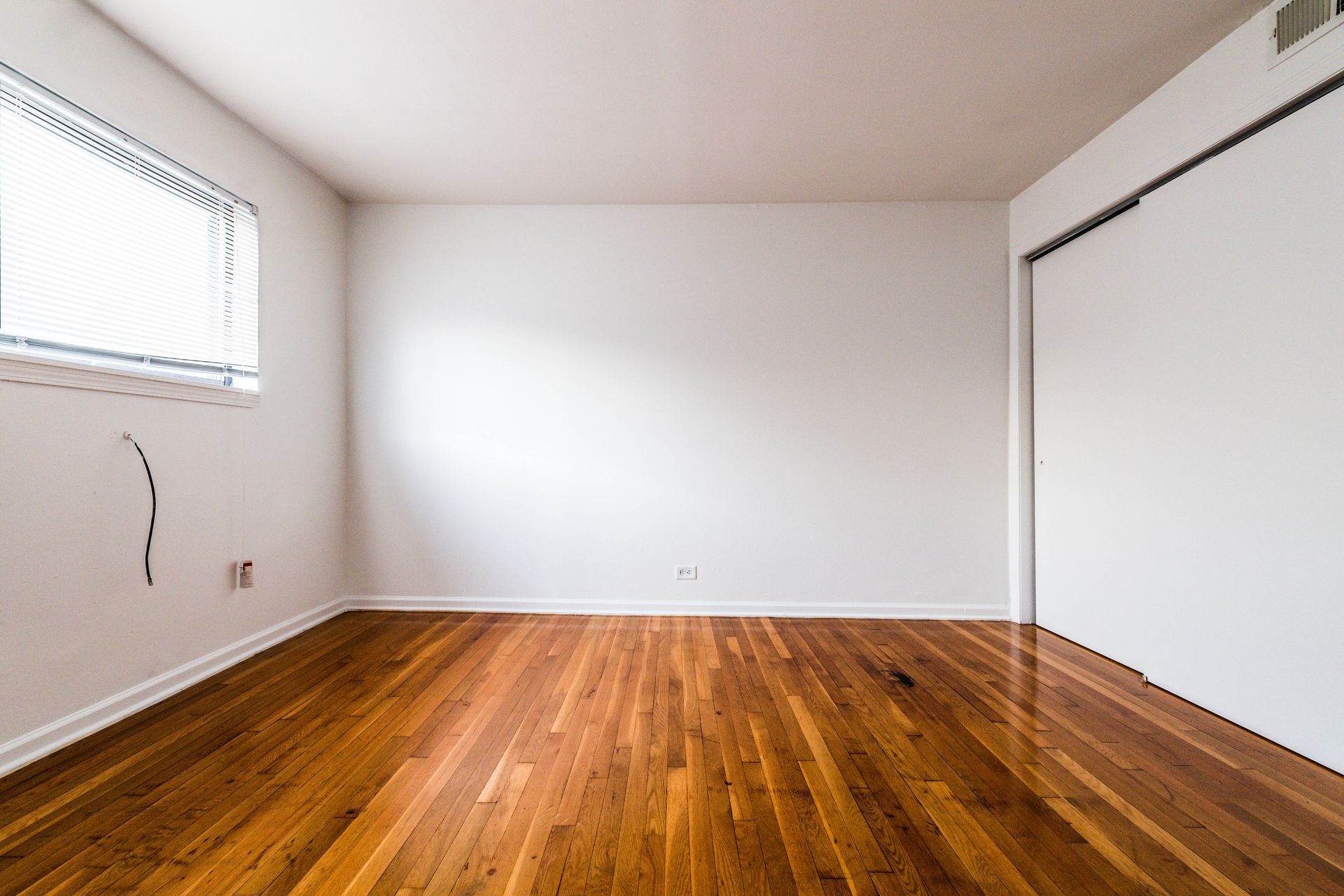 Empty room with hardwood floors, white walls, closet, and a window with blinds.