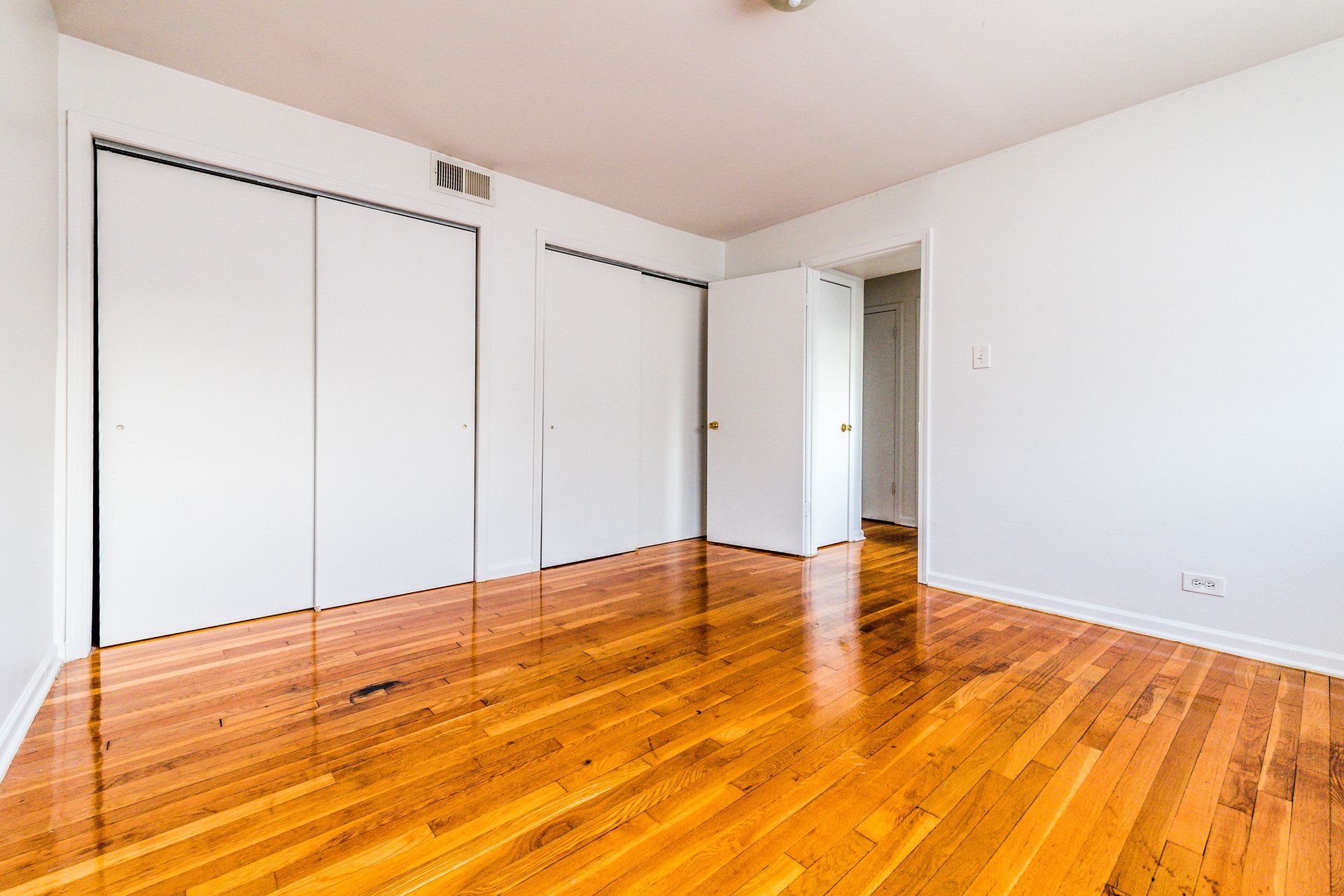 Empty room with hardwood floors, white walls, two closets, and a doorway.