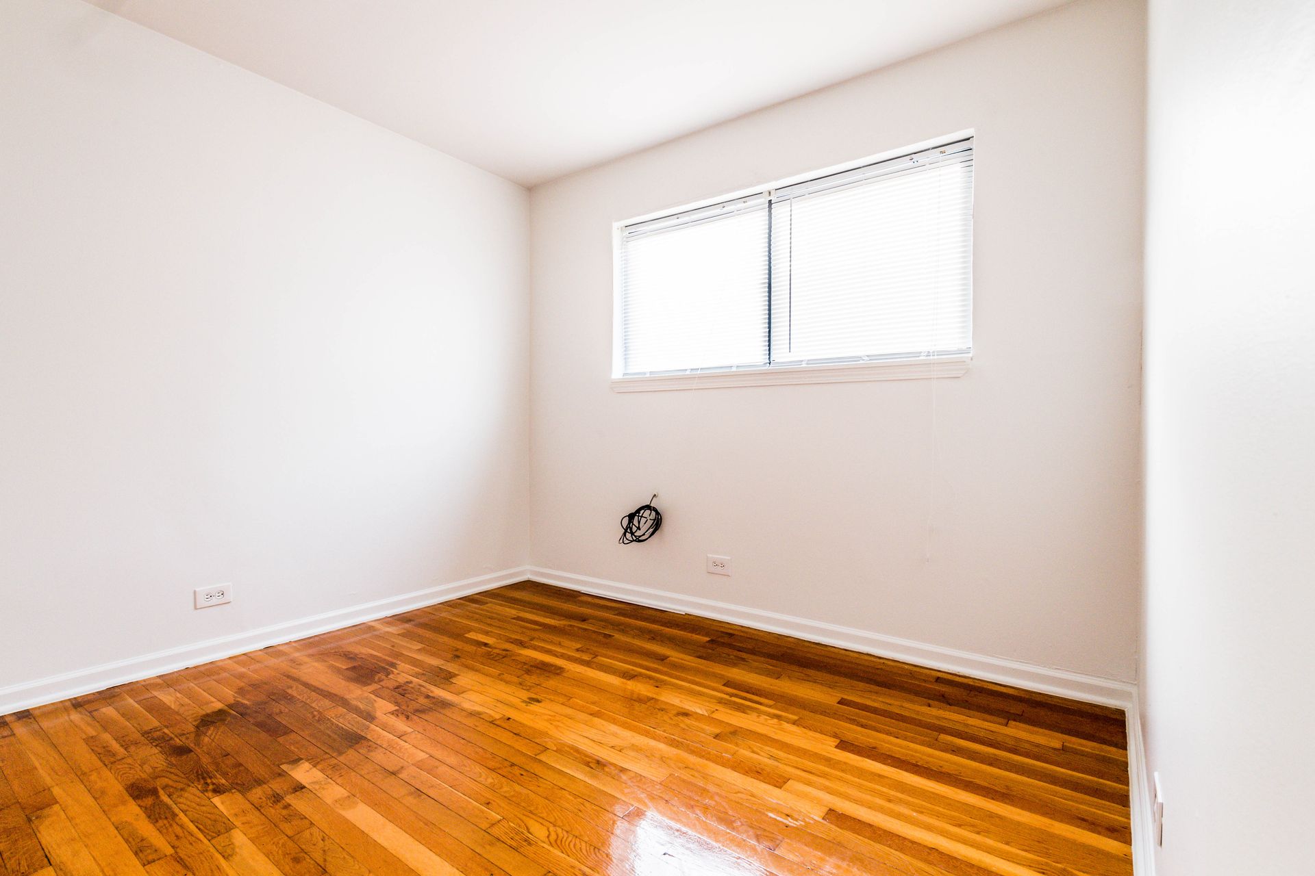 Empty room with hardwood floors, white walls, and a window.