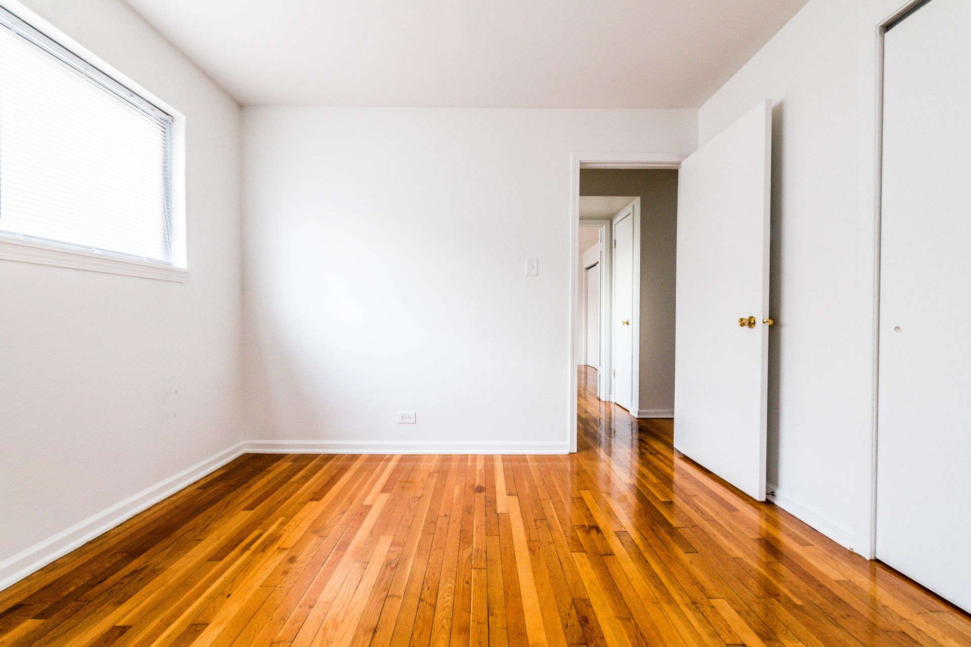 Empty room with hardwood floors, white walls, and a window.