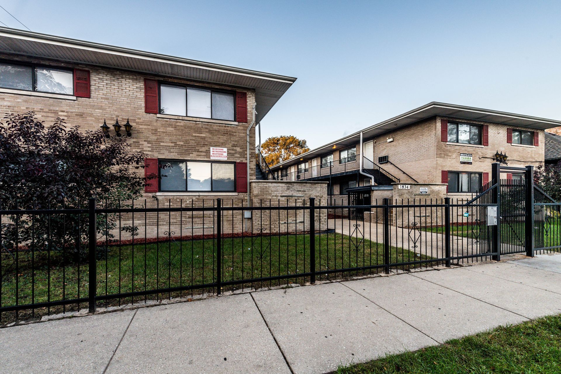 Two-story brick apartment buildings with black fence and sidewalk. Red shutters.