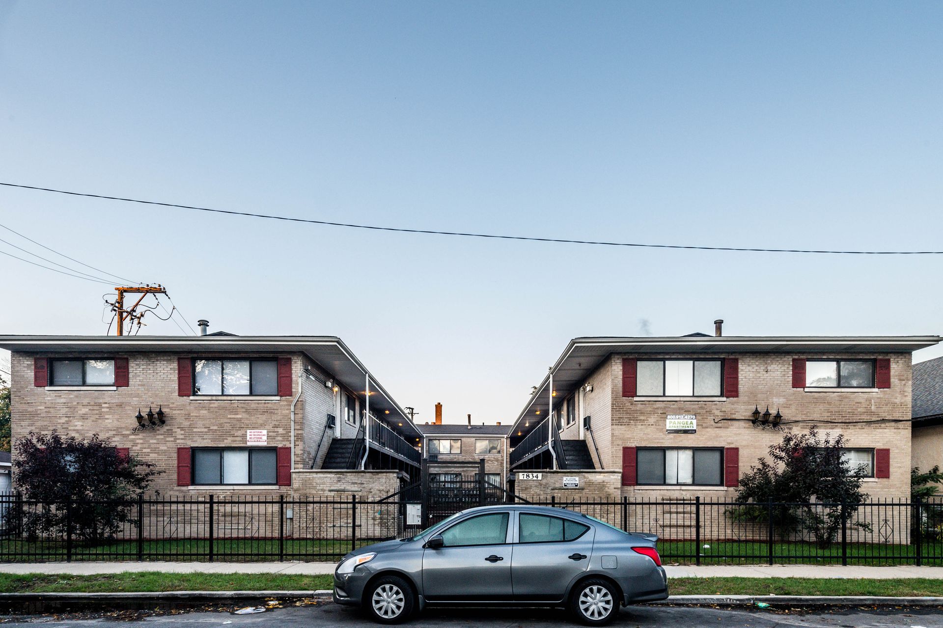 Gray sedan parked in front of two-story brick apartment buildings, under a clear blue sky.