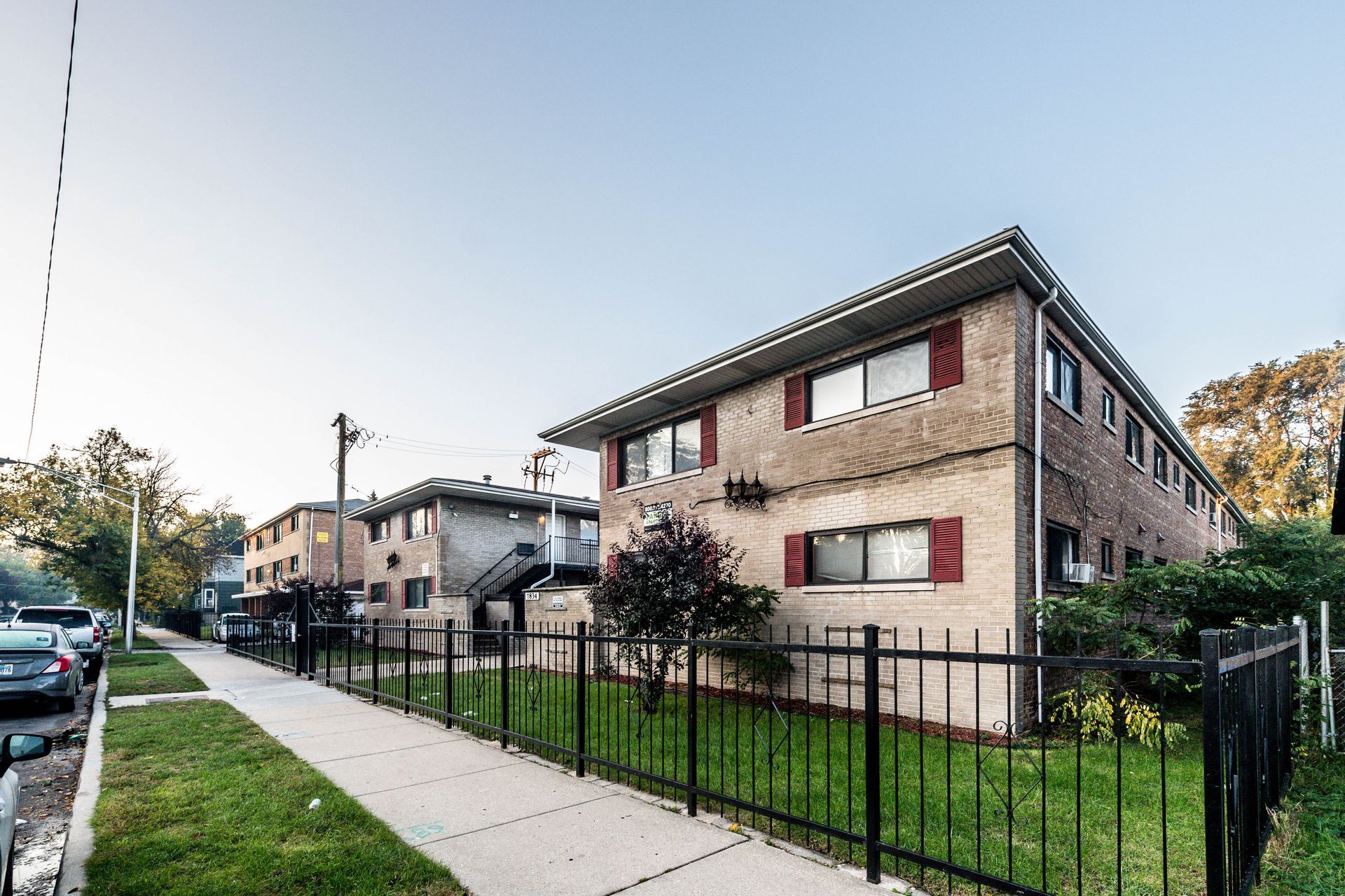 Two-story brick apartment buildings with black iron fence and sidewalk along a residential street.