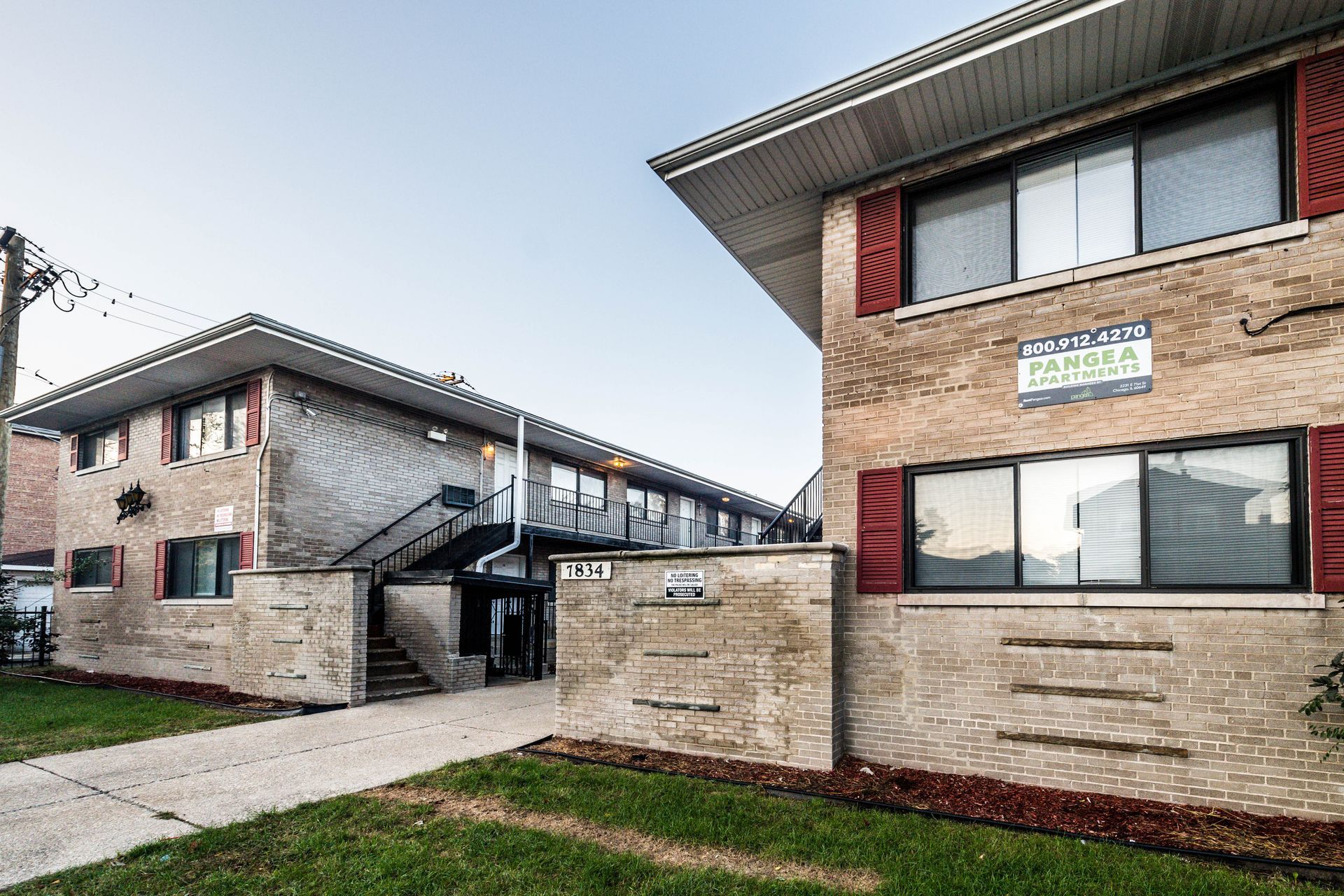 Two-story brick apartment buildings, beige brick, red trim, walkway, and green grass.