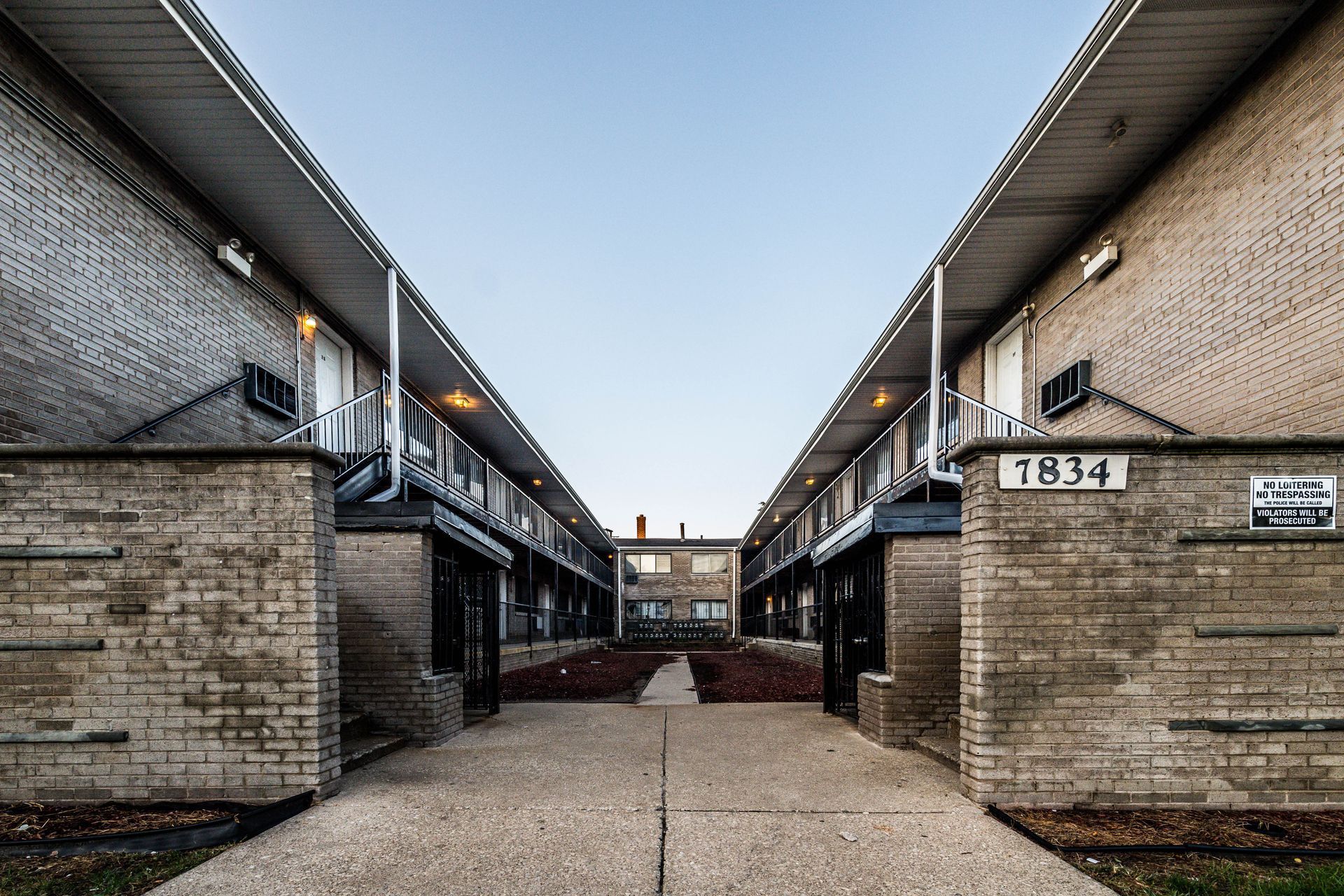 Two-story brick apartment buildings facing each other, connected by a walkway and centered entrance.