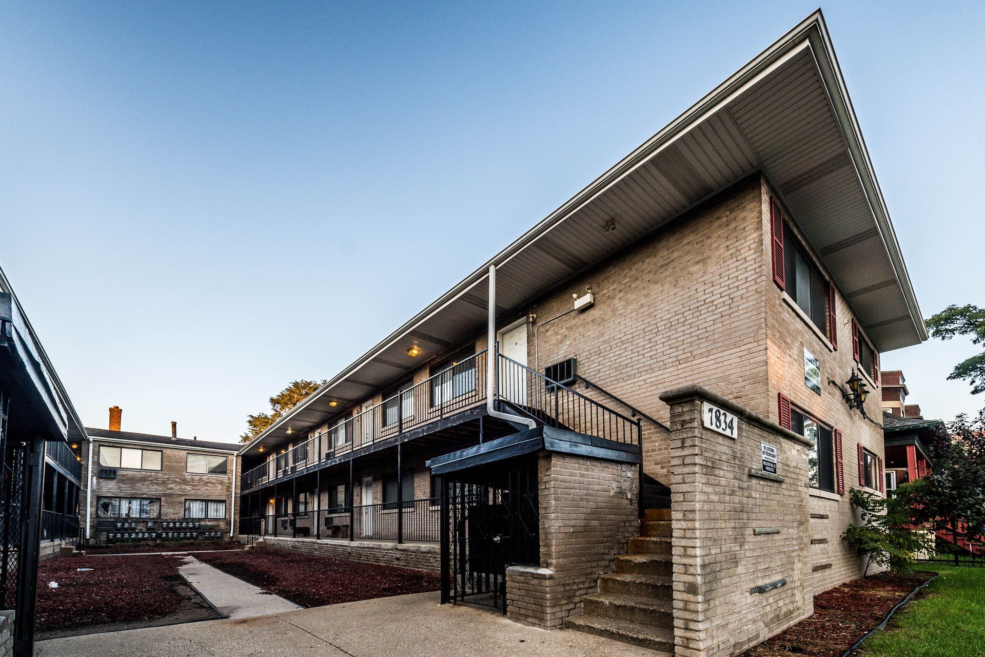 Two-story brick apartment building with blue trim, steps, and black gate.