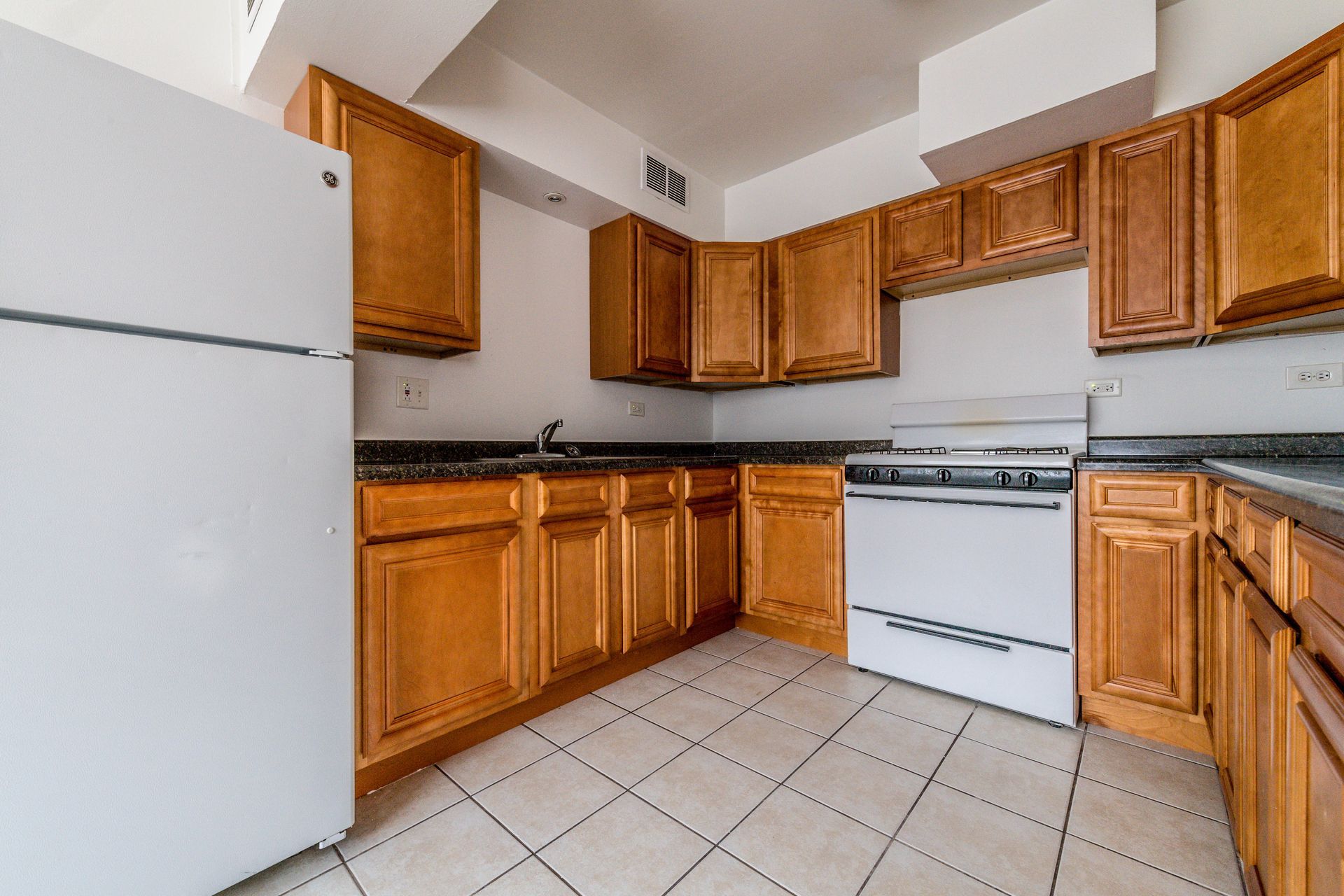 Kitchen with wood cabinets, white appliances, and tiled floor.