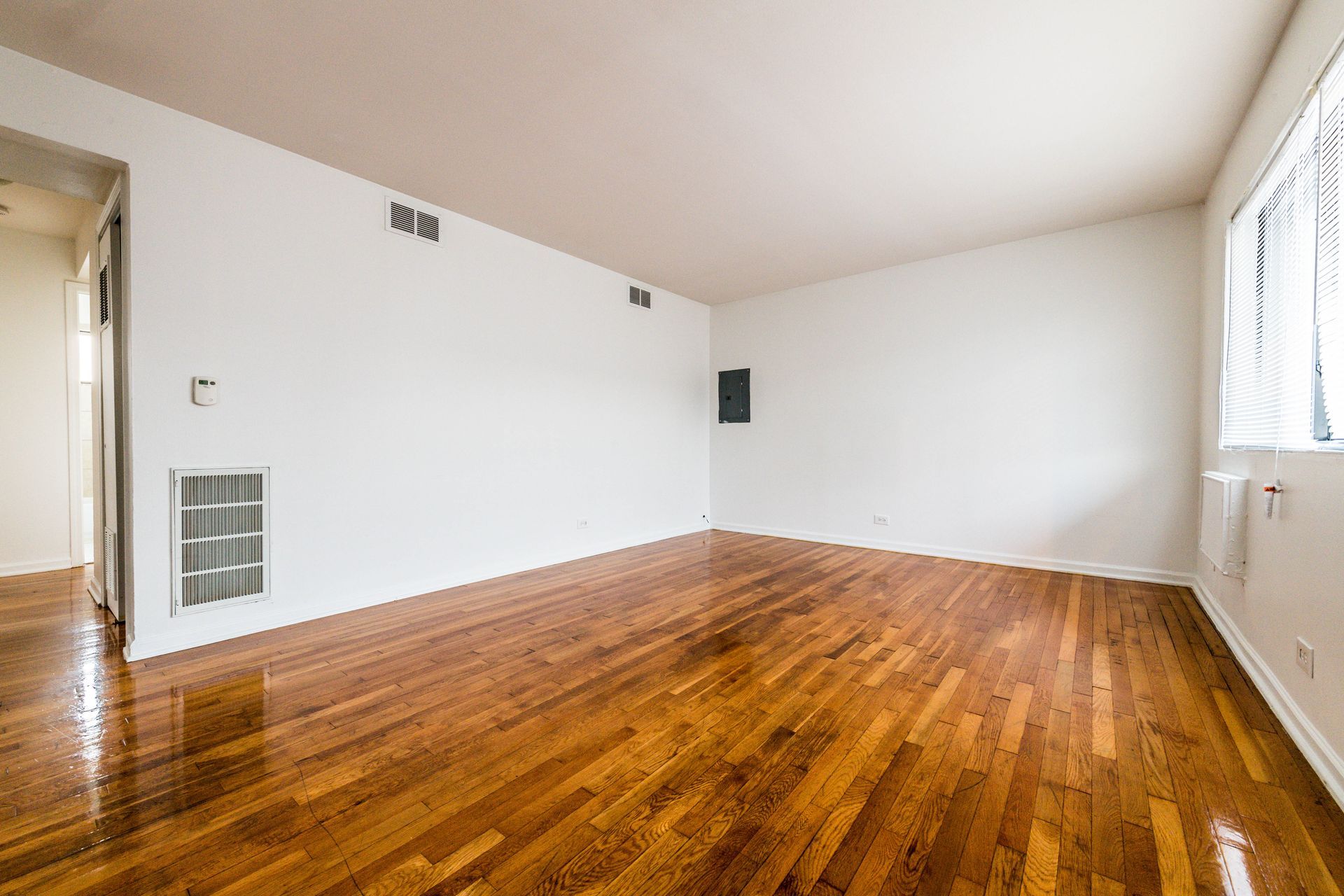 Empty living room with hardwood floors and white walls; window on right.