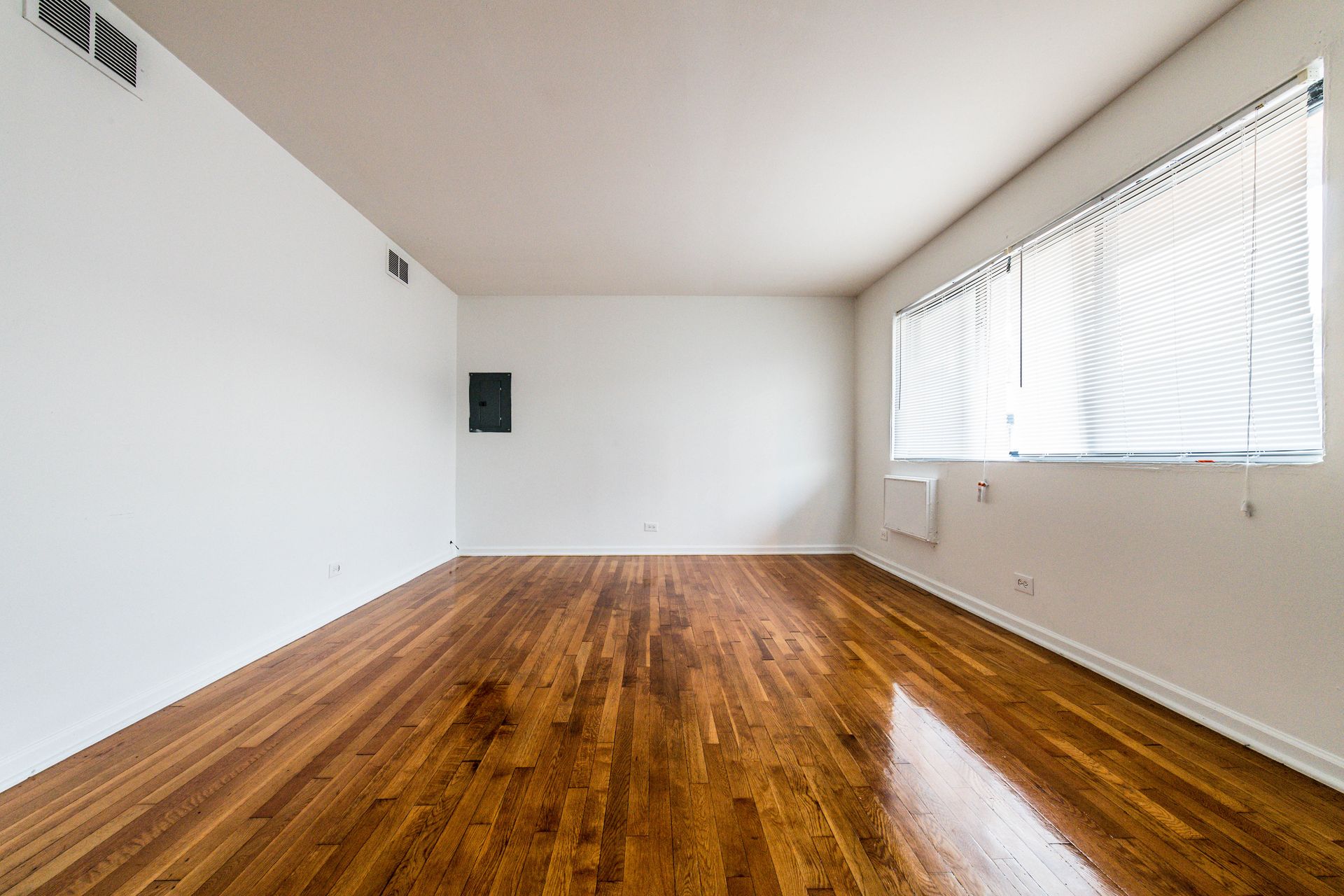 Empty room with hardwood floors, white walls, and a window with blinds.