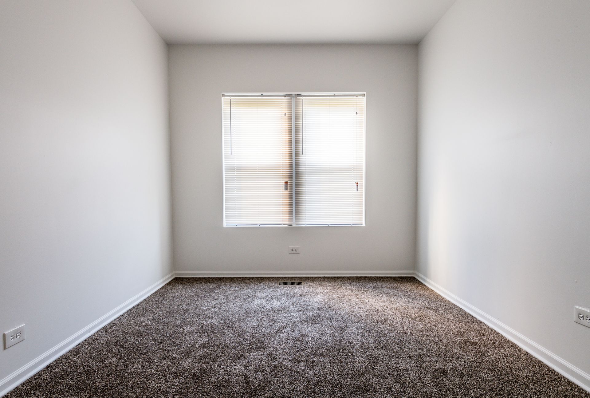 Empty room with brown carpet, white walls, and a window with blinds.