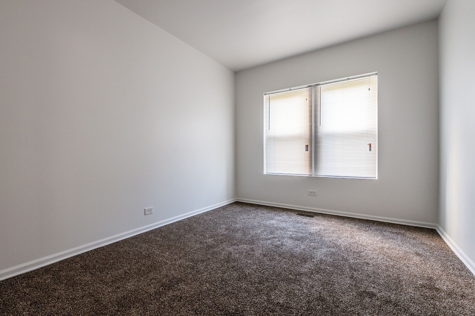 Empty room with brown carpet, white walls, and a window with closed blinds.