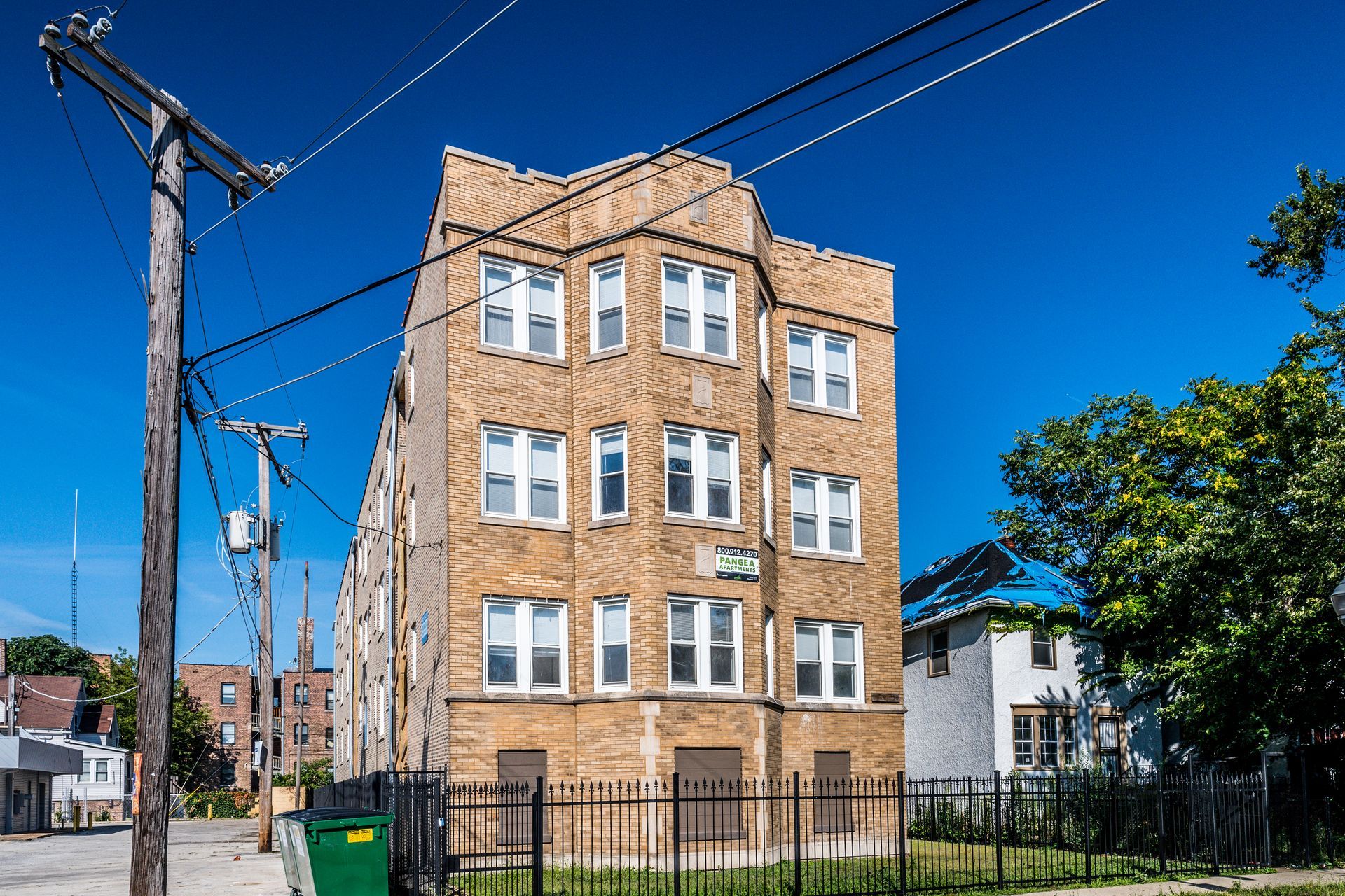 Multi-story brick building with multiple windows under a blue sky, fence in foreground.