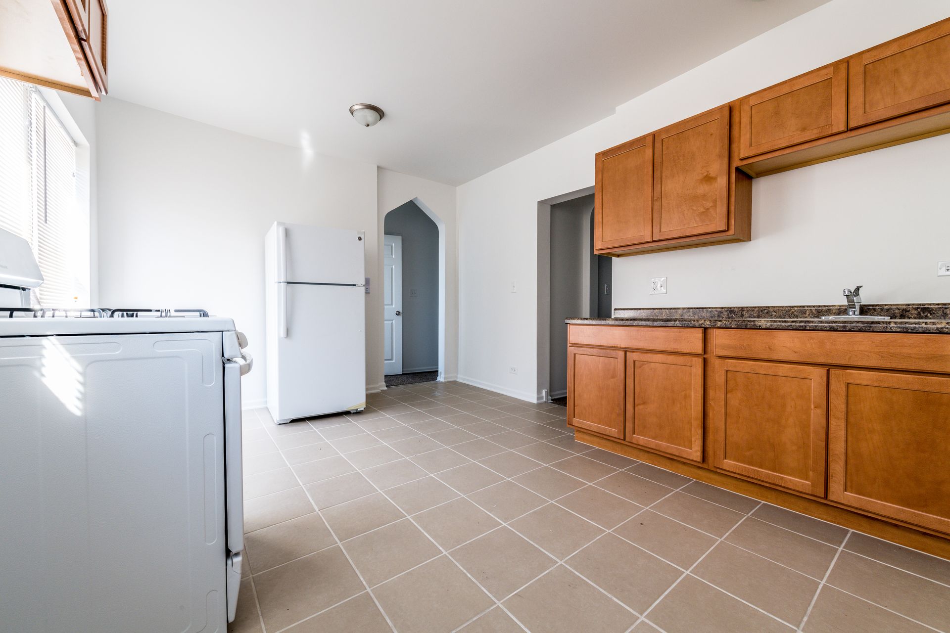 Kitchen with white appliances, wooden cabinets, and tile floor.