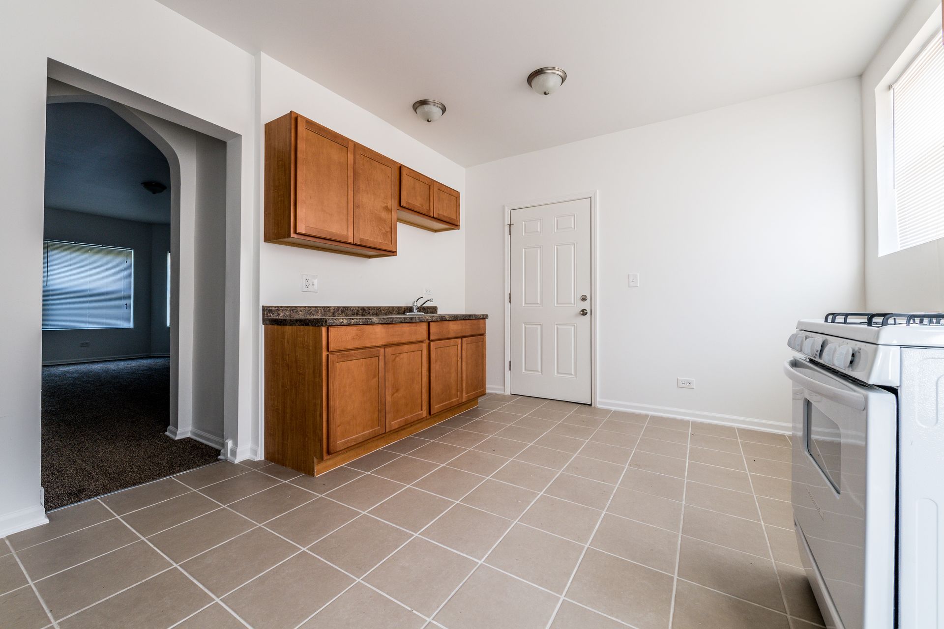 Empty kitchen with brown cabinets, white stove, and tile floor.