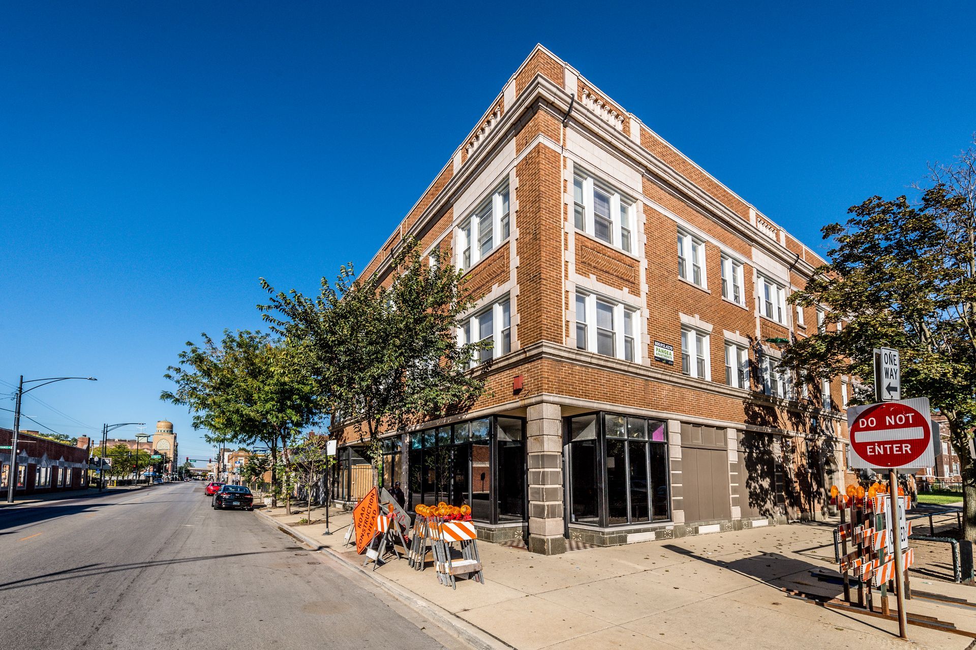 Three-story brick building on a street corner, with retail space on the ground floor. Blue sky.