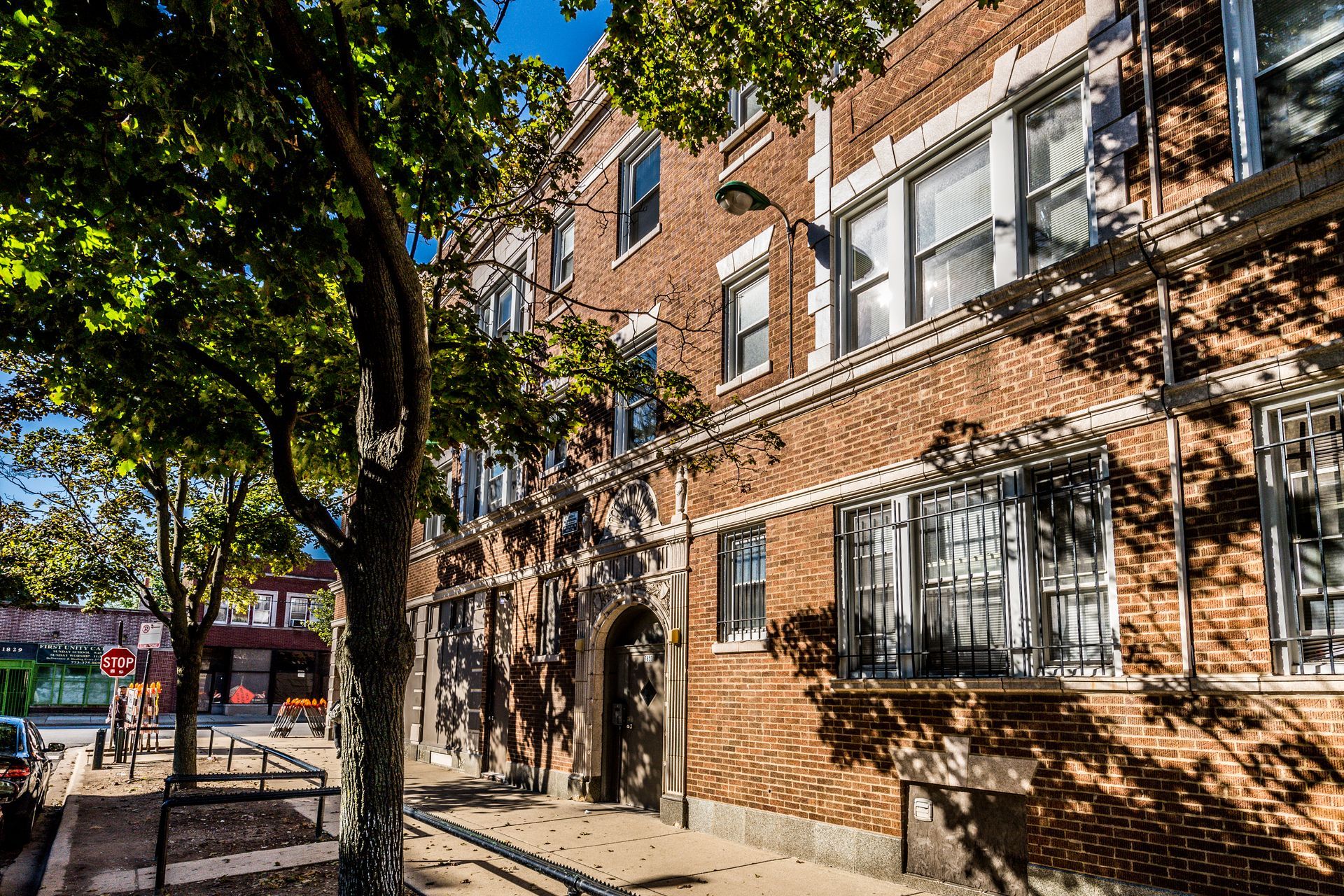 Brick apartment building with trees, sidewalks, and street on a sunny day.