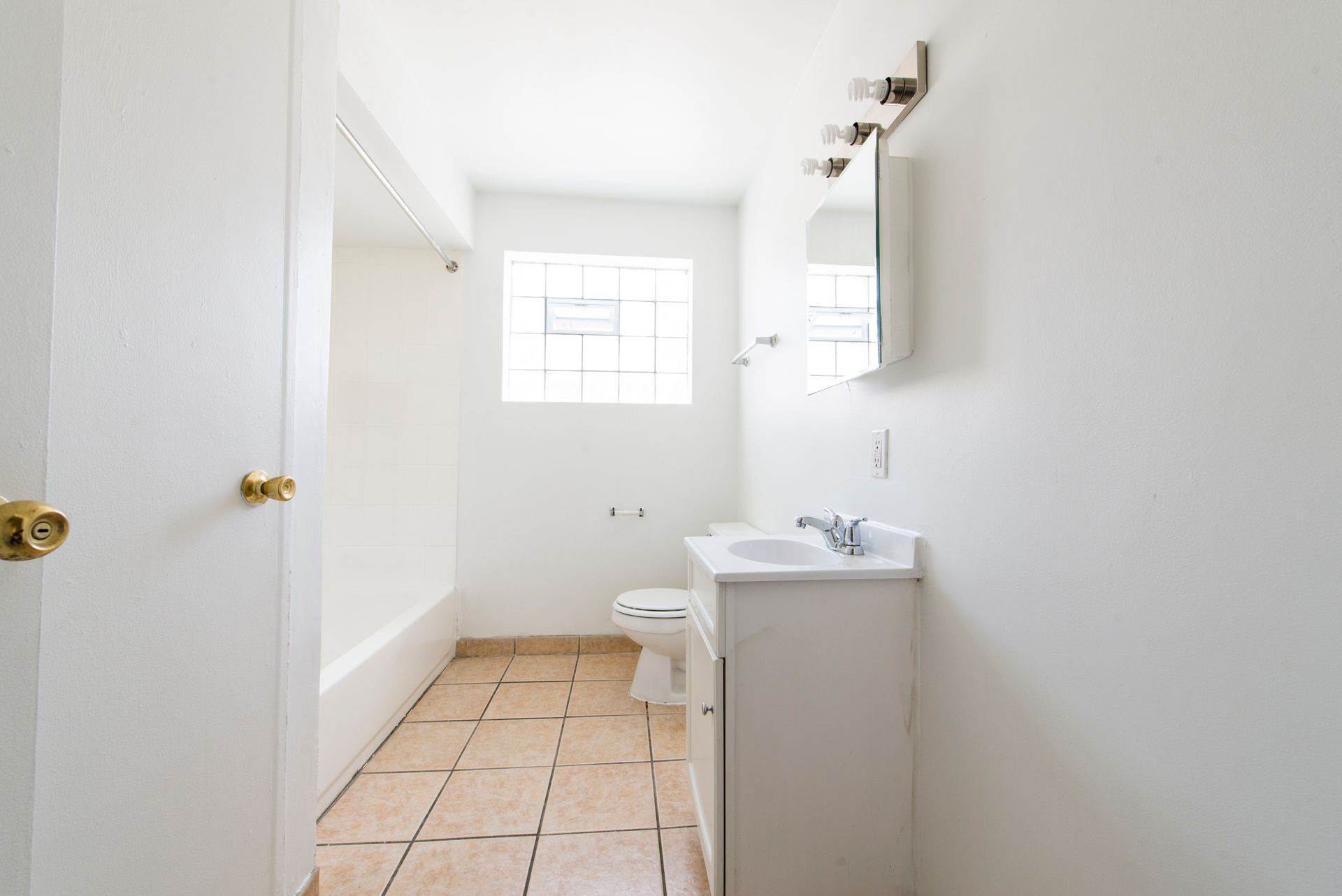 Bathroom with white walls, tiled floor, bathtub, sink, toilet, and a window.