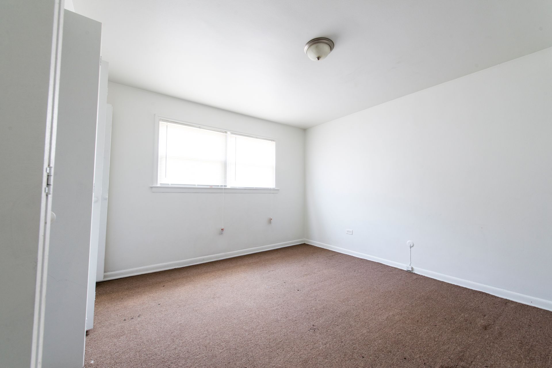 Empty white room with a window, brown carpet, and a white closet door.