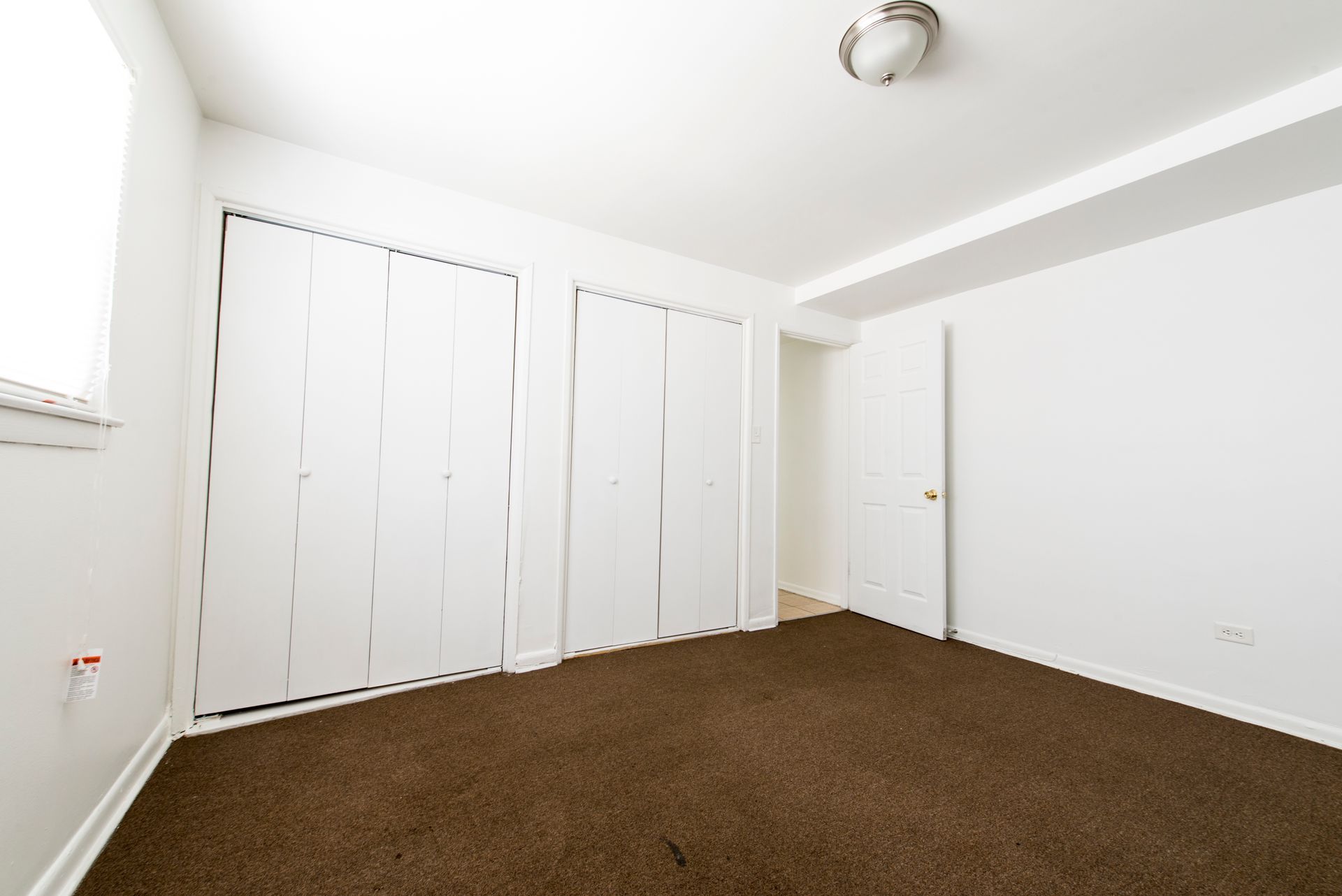 Empty bedroom with brown carpet, white walls, and closet doors.