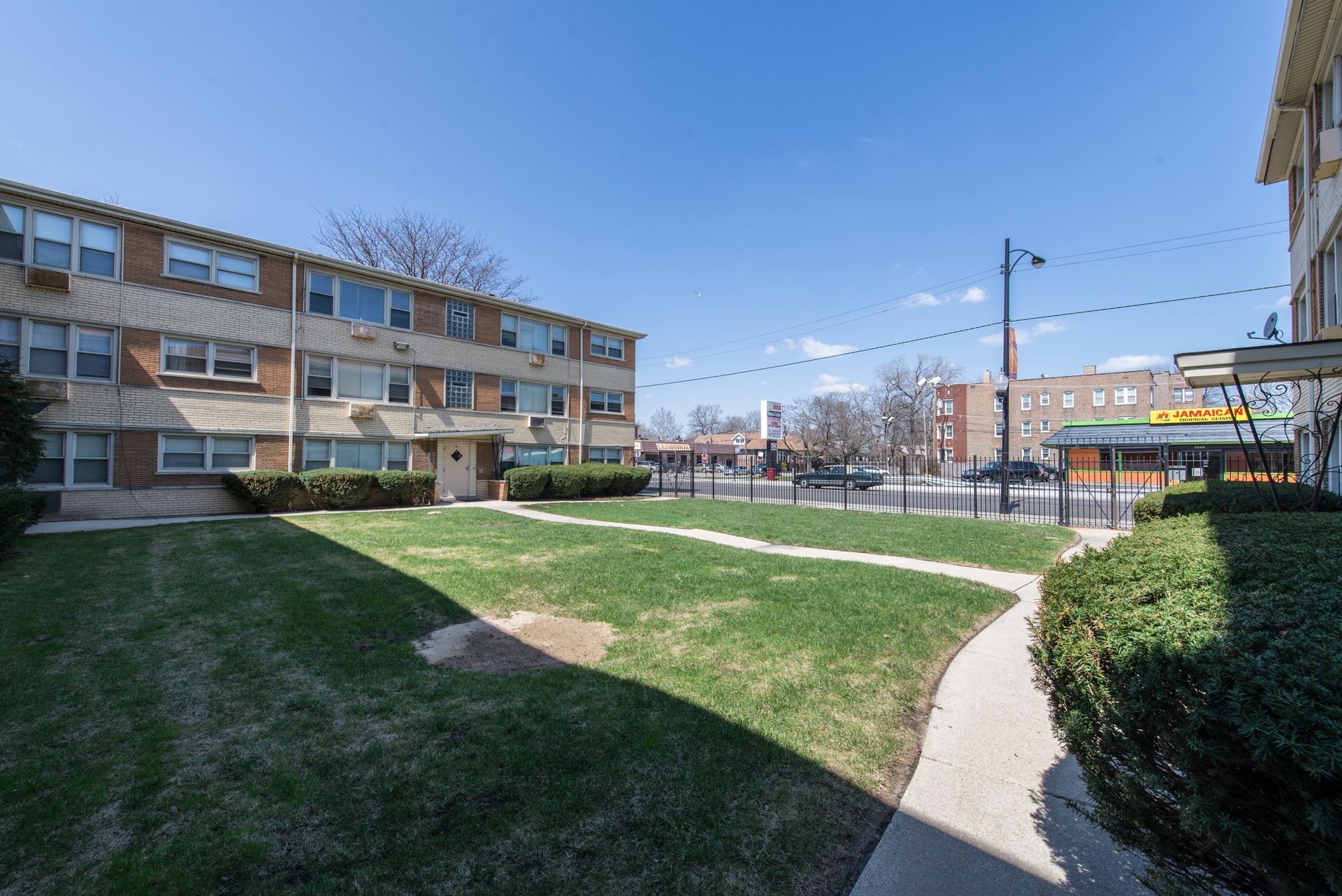 Two-story brick apartment buildings flank a small grassy courtyard with a sidewalk and street beyond.