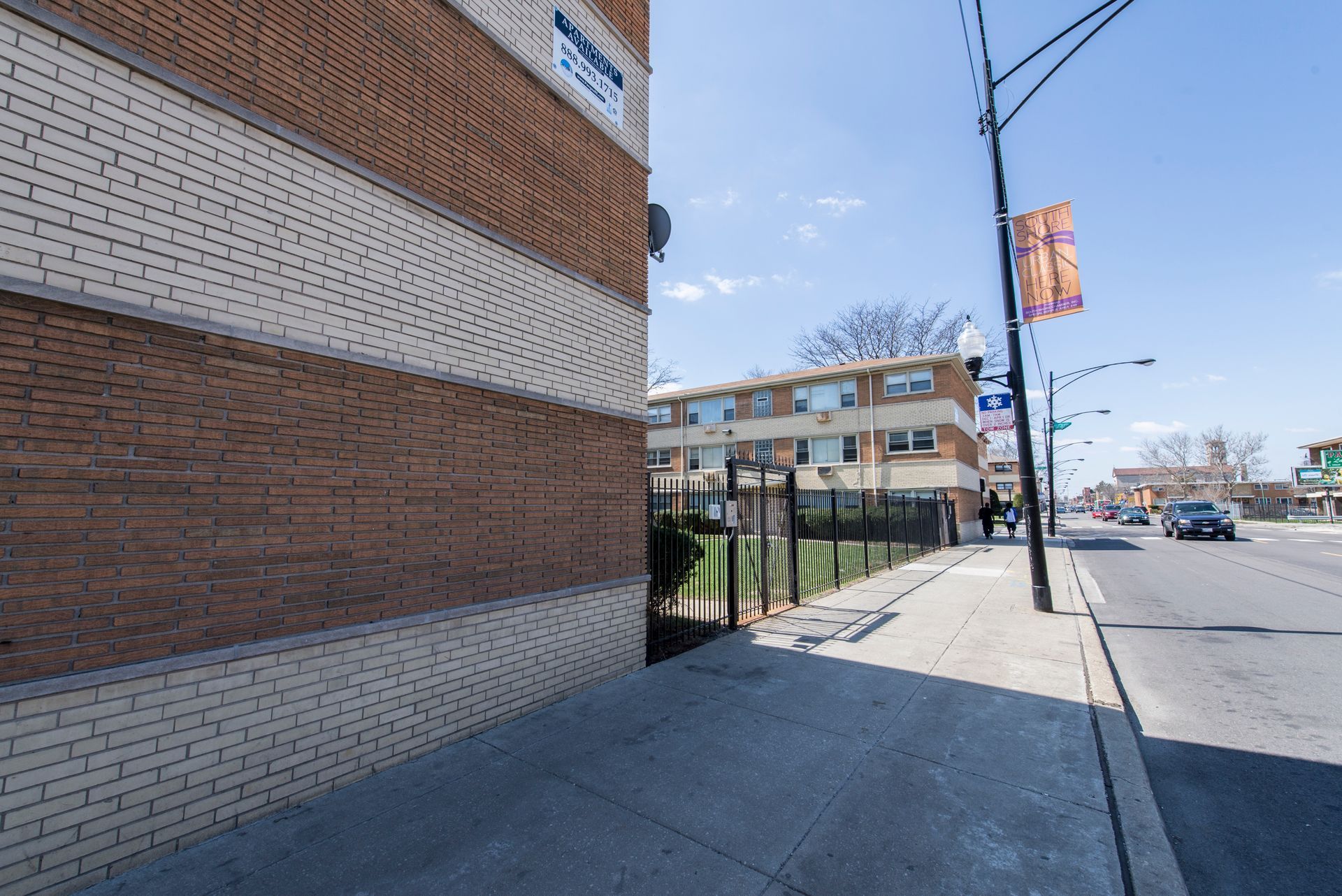 Brick building corner, sidewalk, street, two-story building, blue sky, two banners, car.