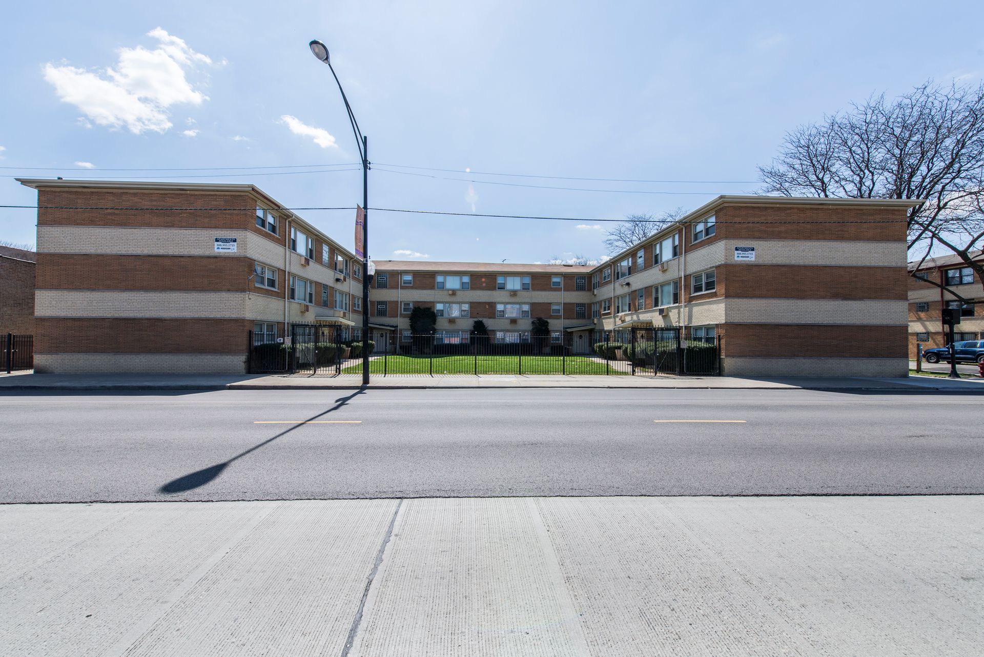 Brick apartment building with rows of windows and a central courtyard, viewed from across a street.