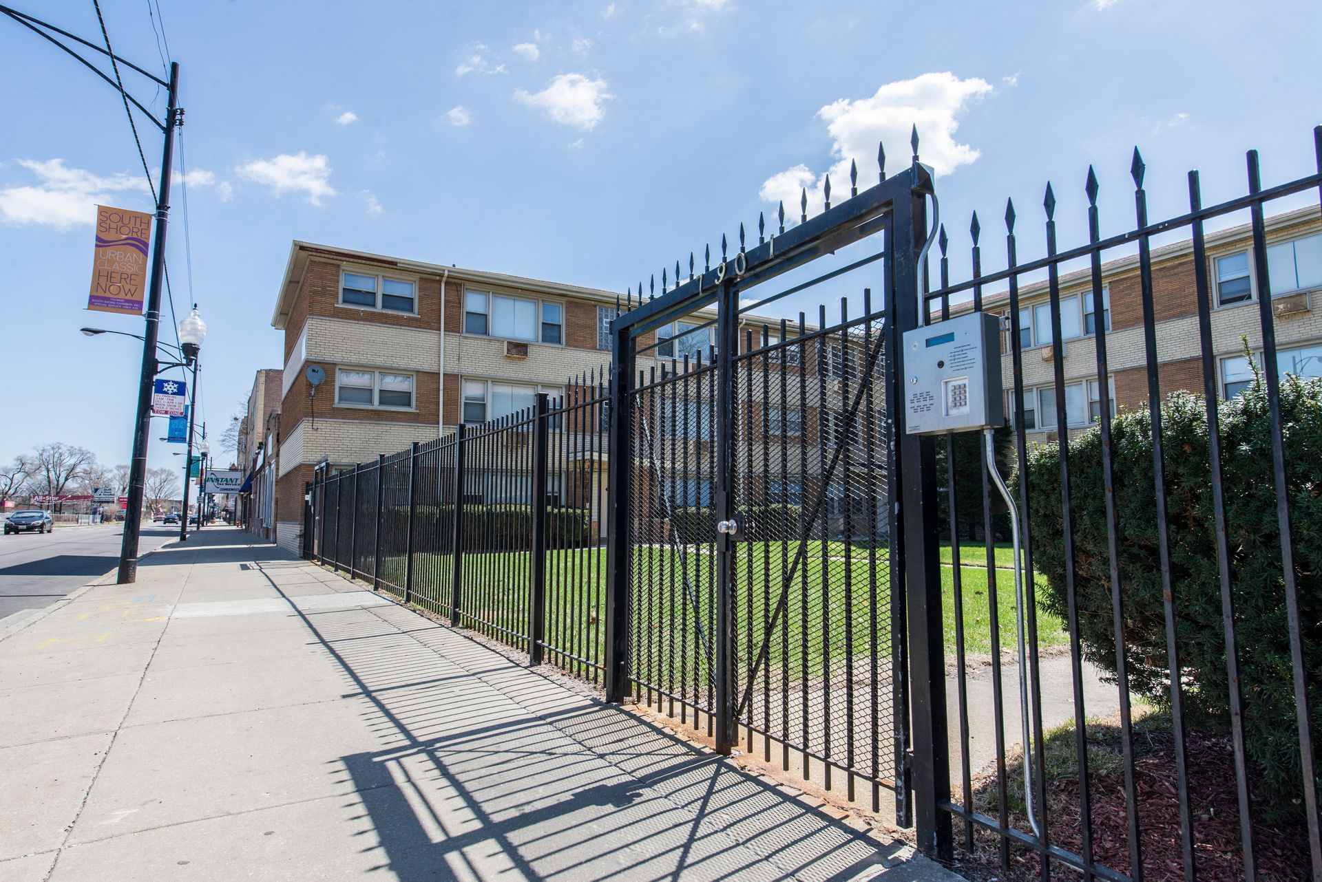 Black metal gate and fence in front of a brick apartment building on a city street.