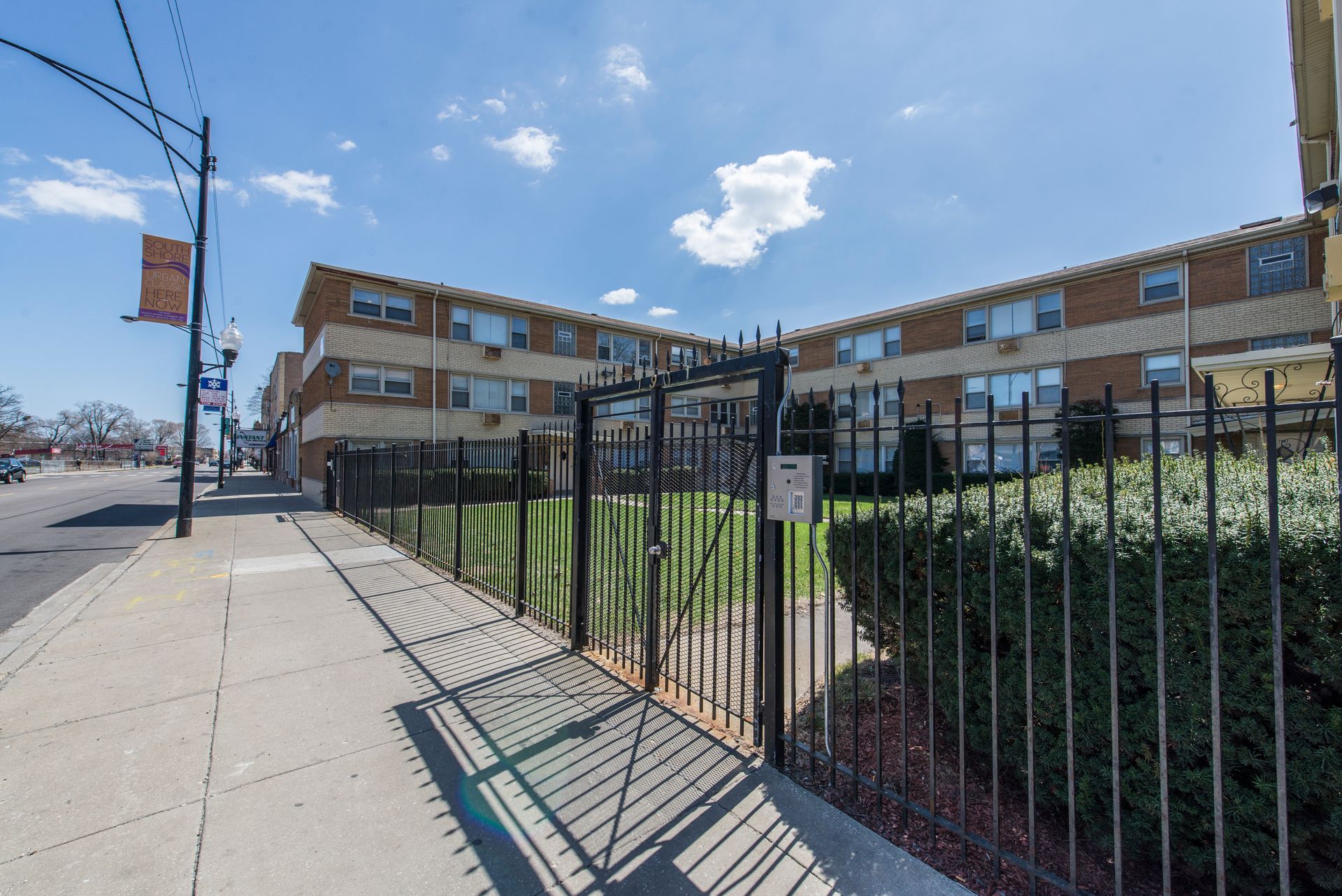 Apartment building behind a black metal fence on a sunny day.