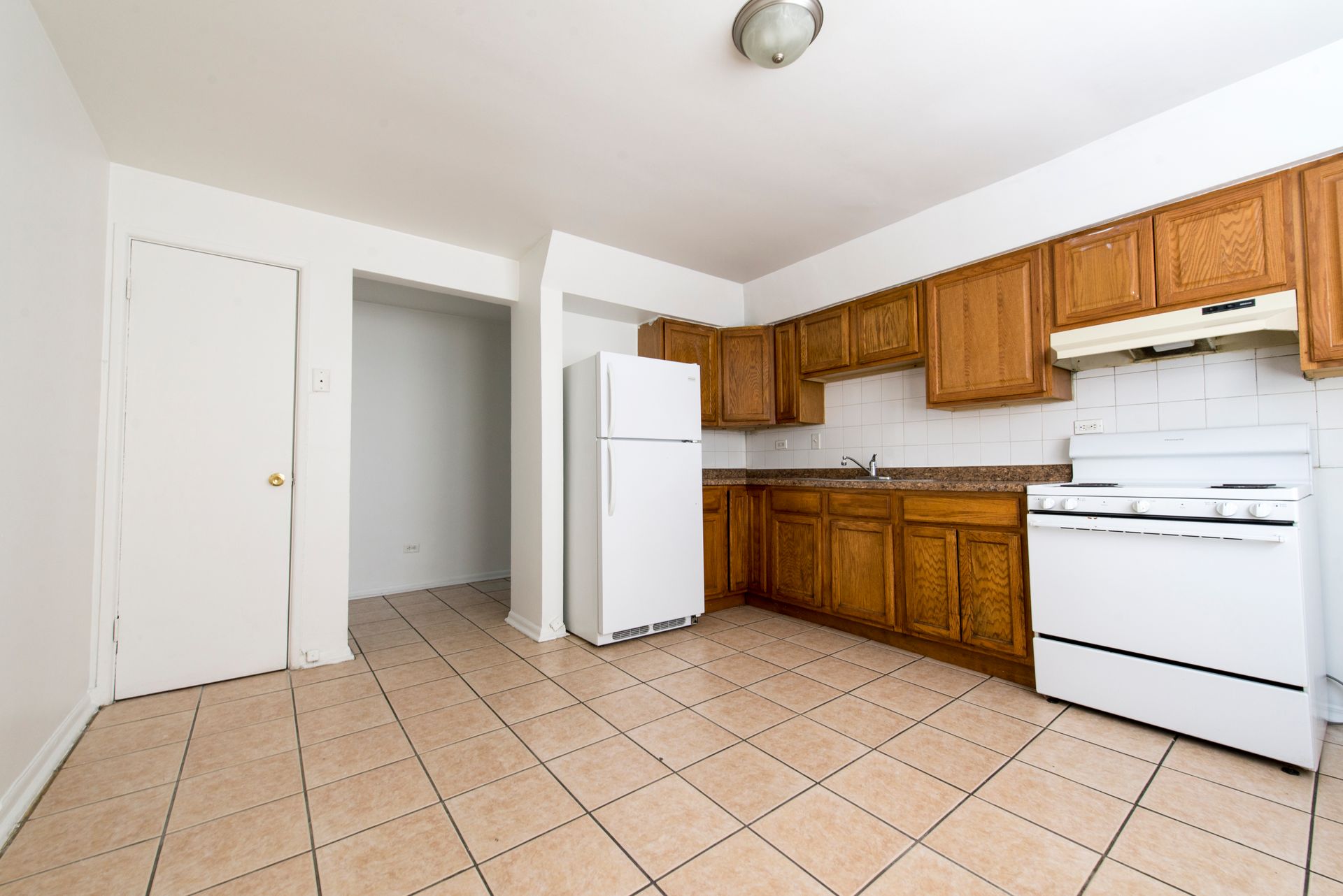 Kitchen with wood cabinets, white appliances, and tiled floor.