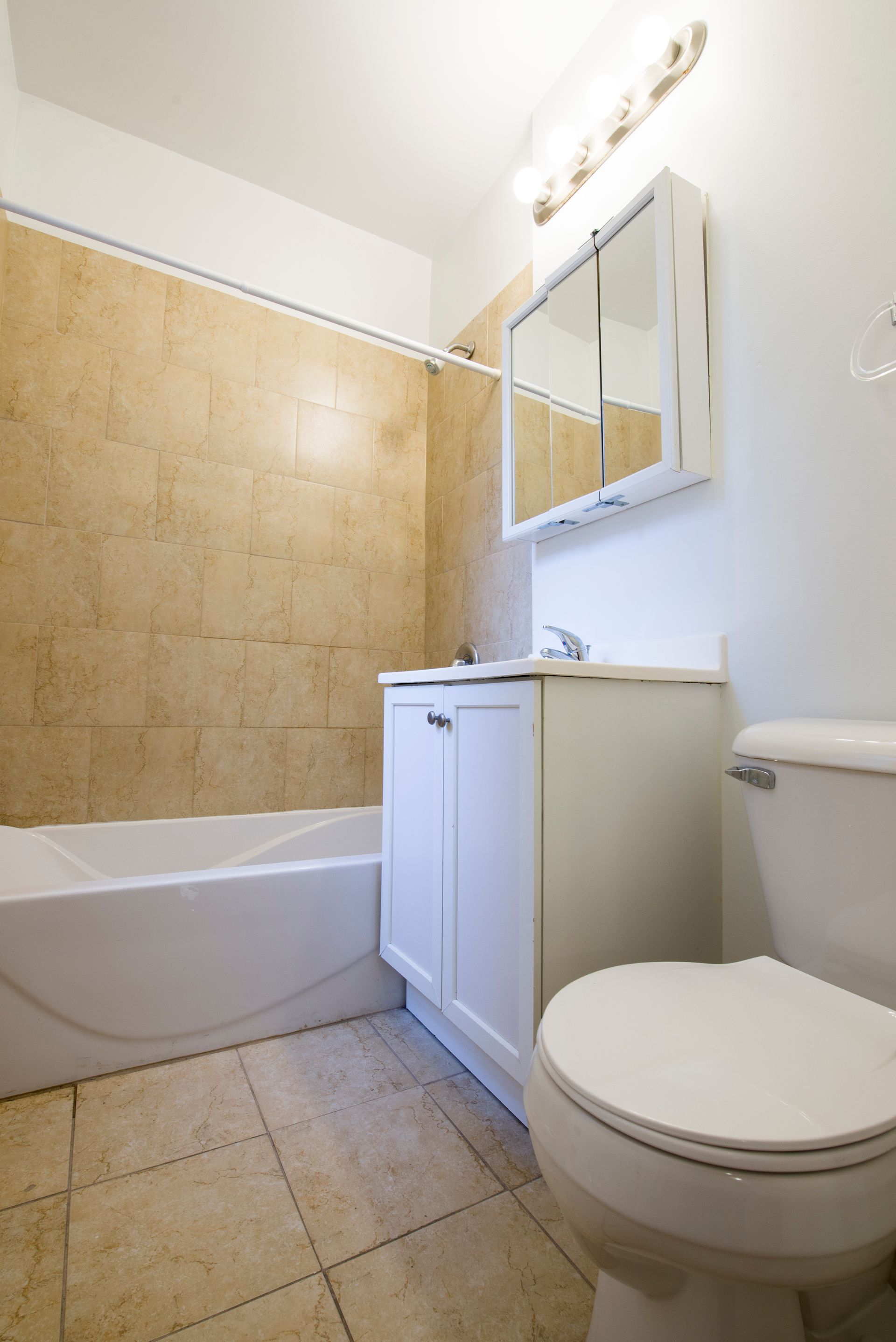 Bathroom with white fixtures, beige tile walls and floor, white vanity cabinet, and mirrored medicine cabinet.