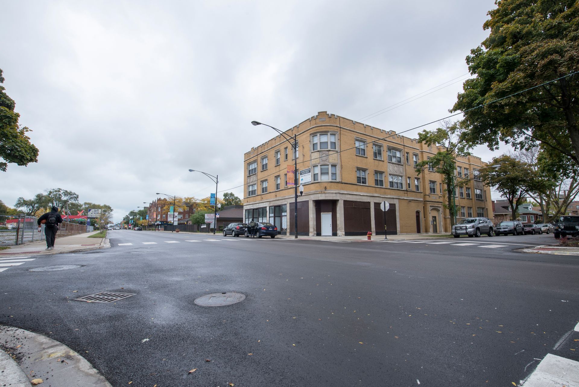 Street corner with a brick building and a person walking. Overcast day.