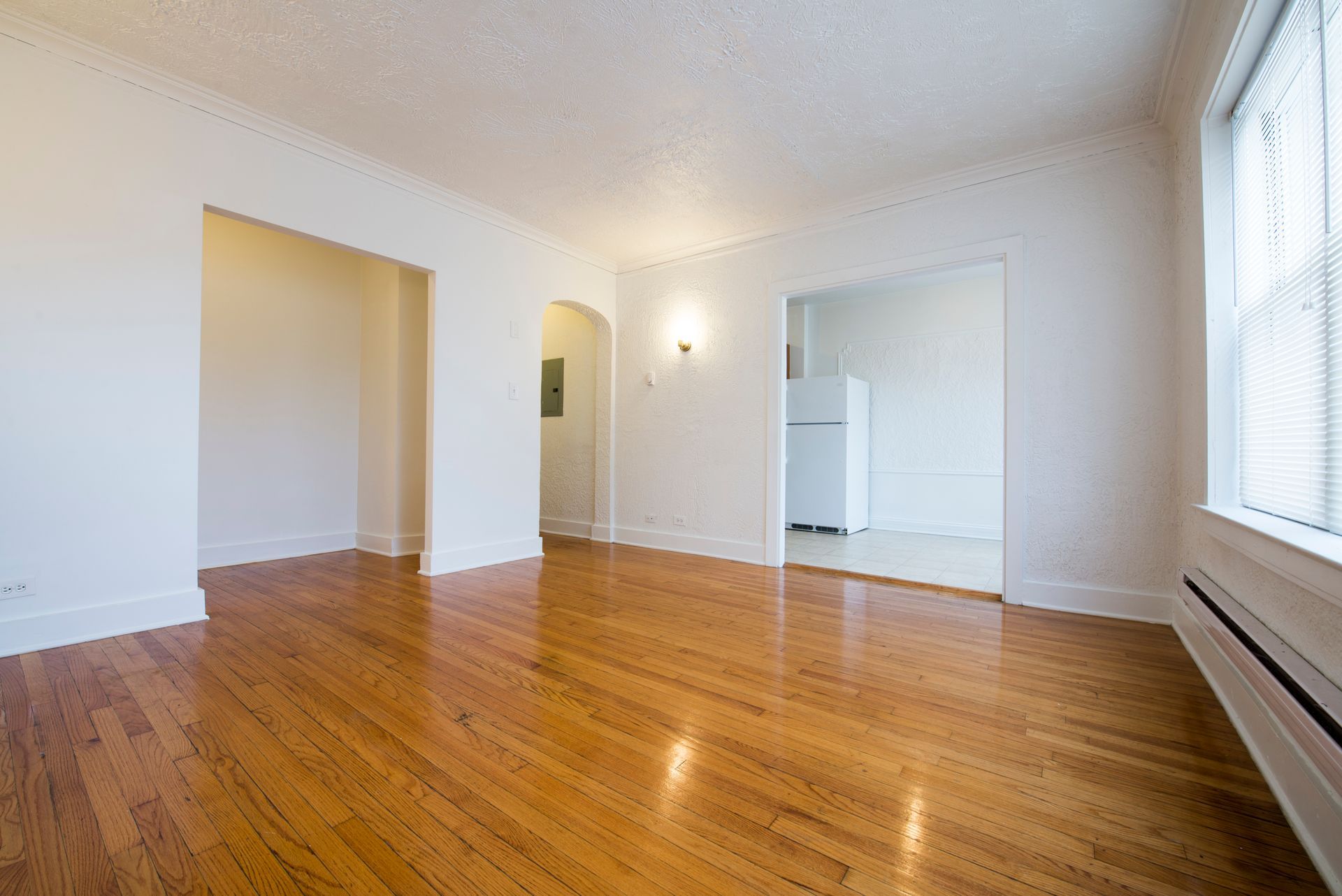 Empty apartment with hardwood floors, white walls, and doorways leading to other rooms.