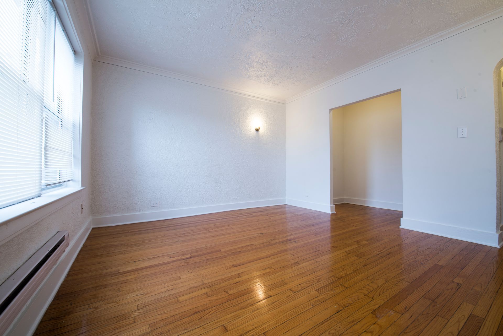Empty room with hardwood floors, white walls, and a window with blinds.