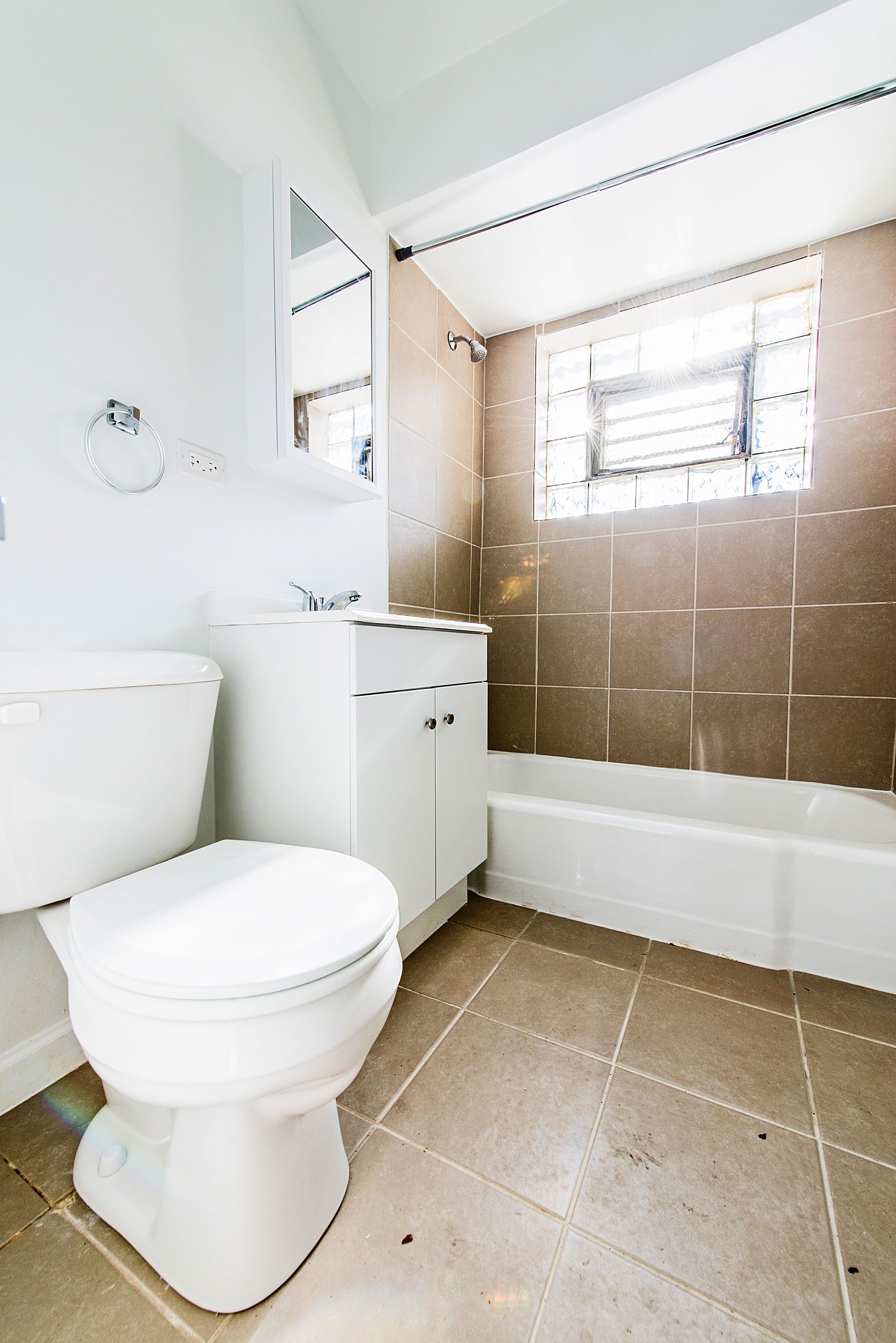 Bathroom with white toilet, vanity, and bathtub, brown tile accent wall, and a window.