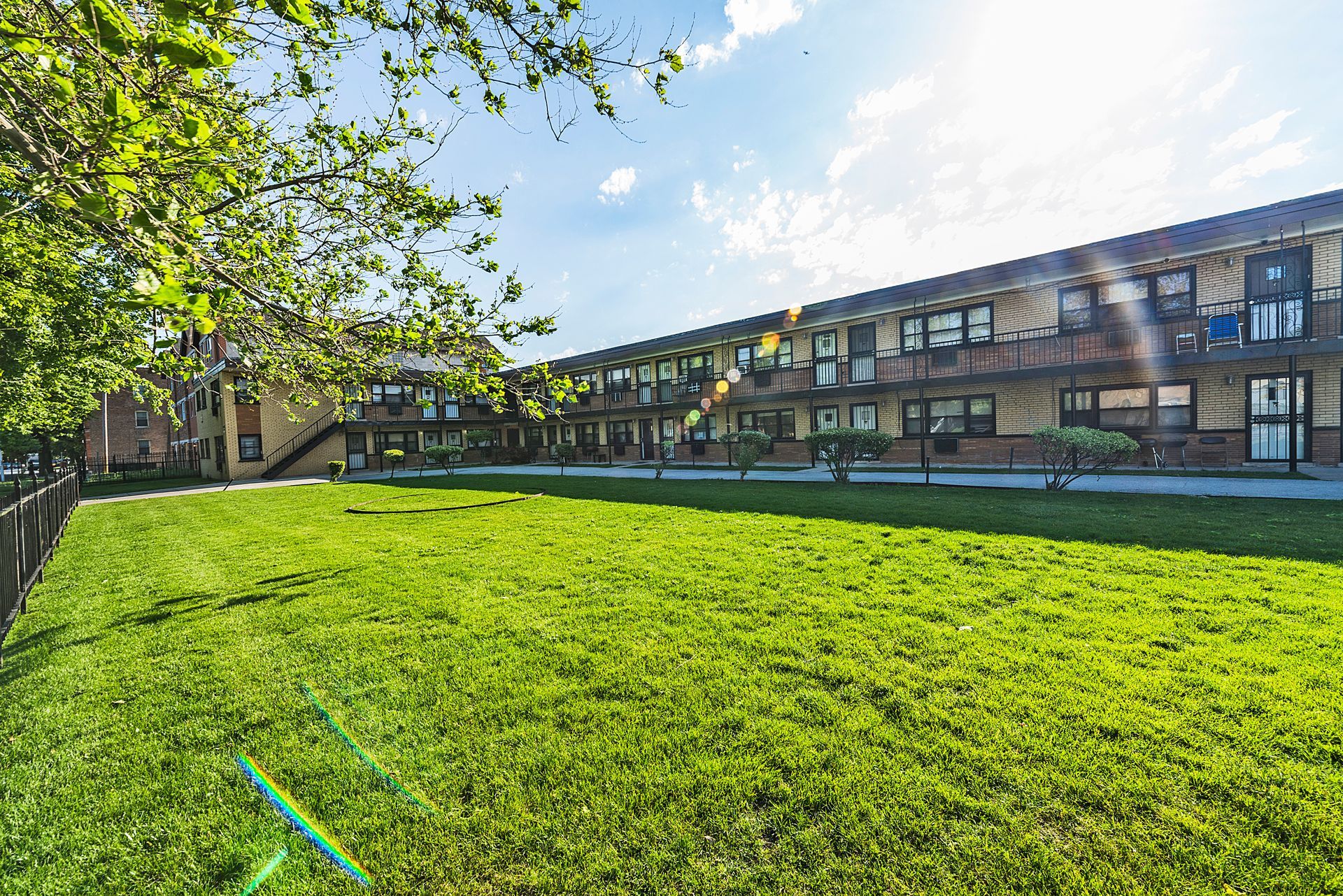 Long, two-story brick apartment building with a large green lawn under a bright, sunny sky.
