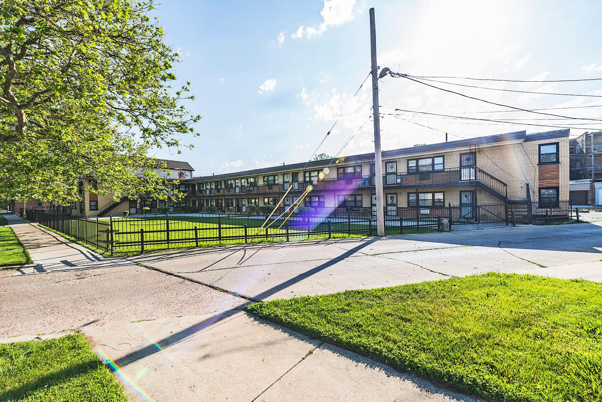 Apartment building with exterior walkways, grass, and a bright sky with power lines.