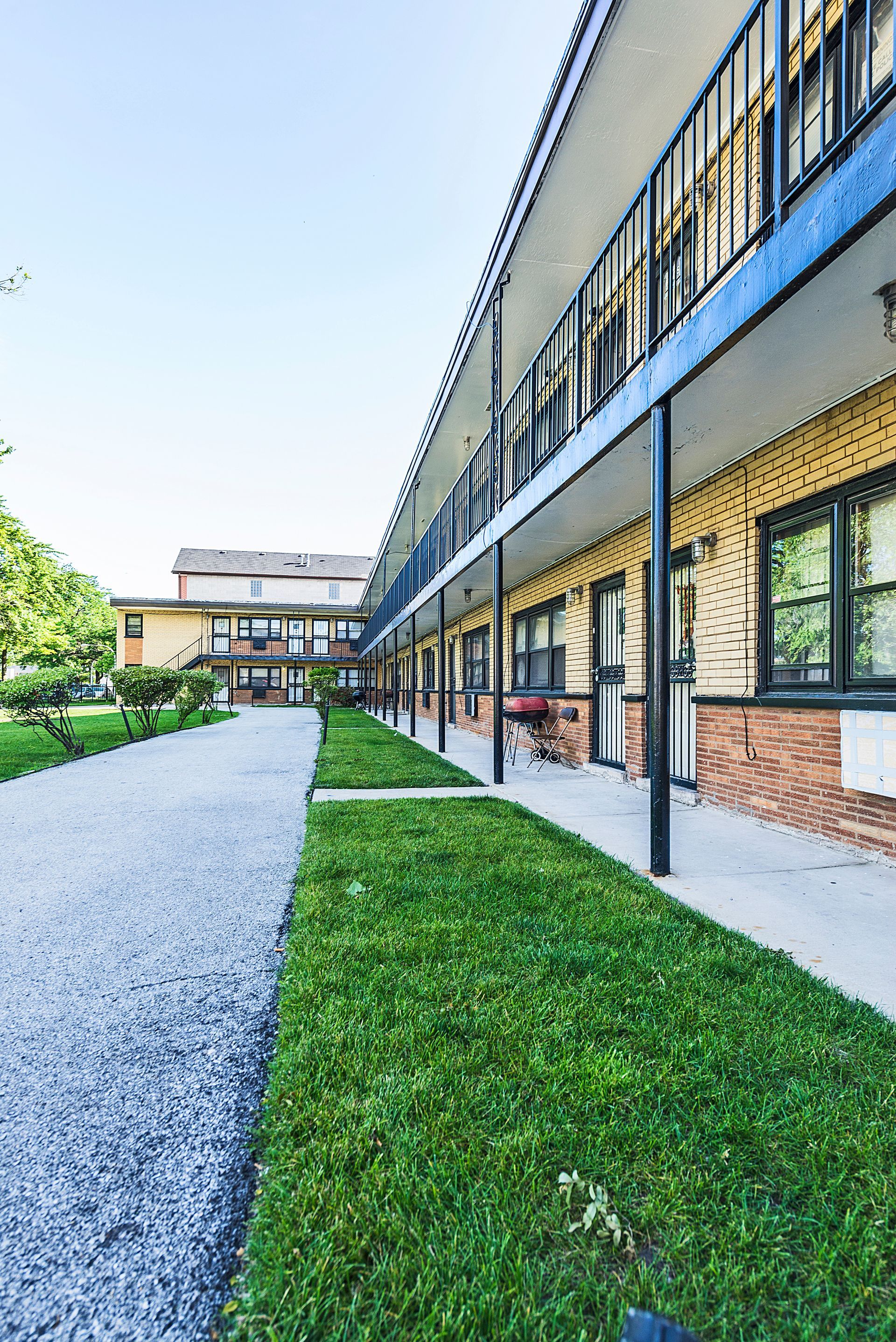 Apartment building with covered walkways, gravel path, and lawn.
