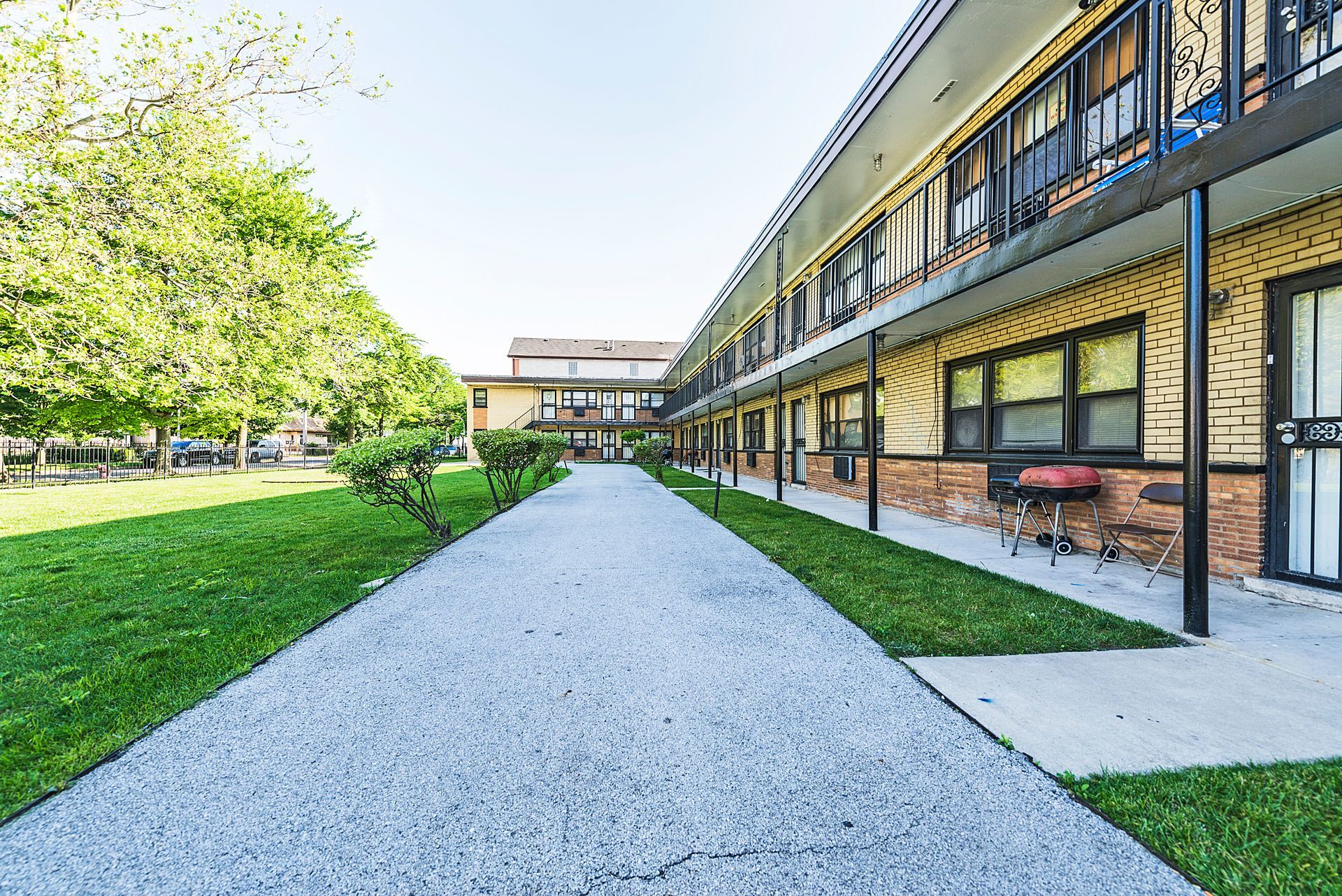 Exterior view of a two-story apartment building with a central walkway and green lawn.