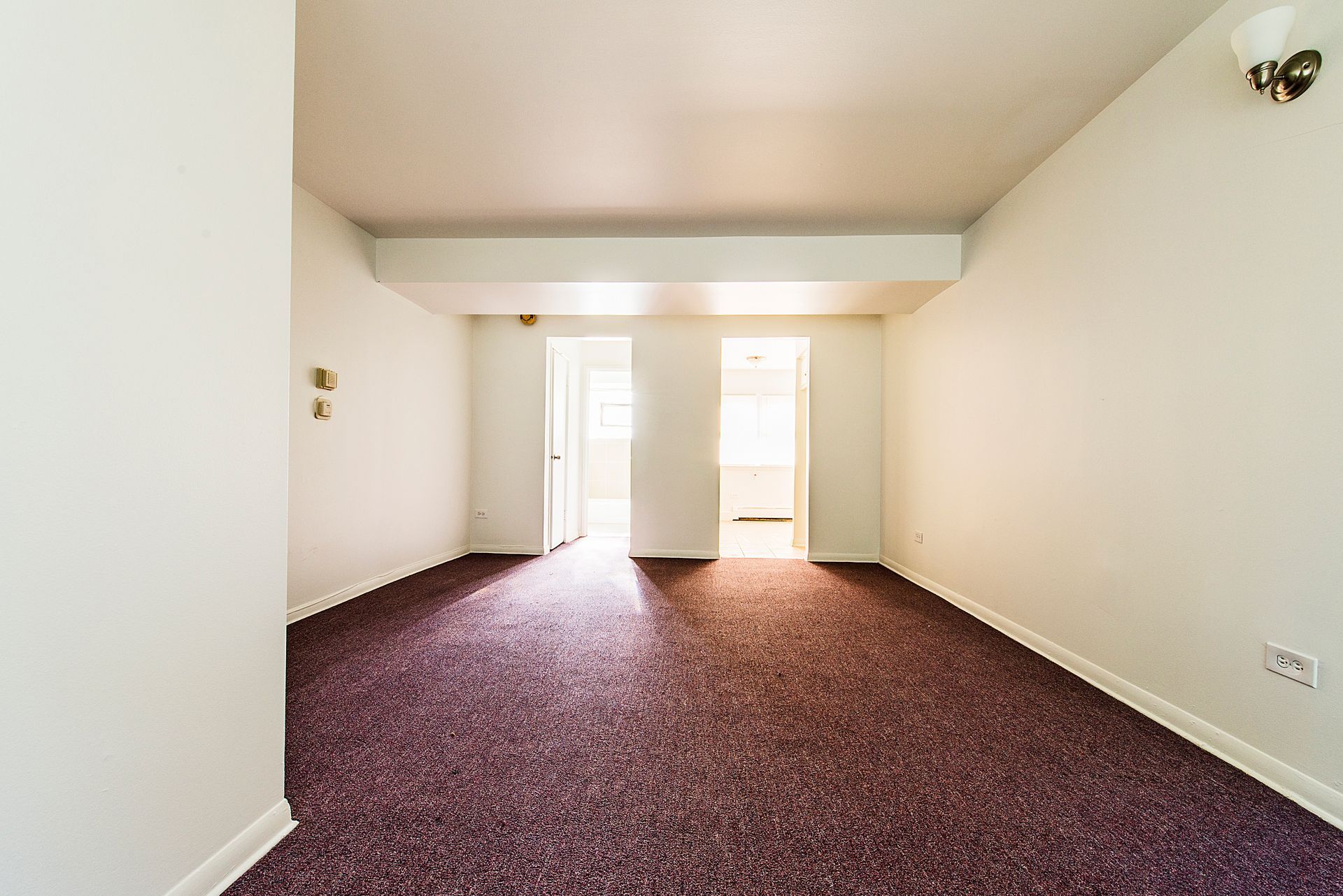 Empty room with burgundy carpet, white walls, and two open doorways.