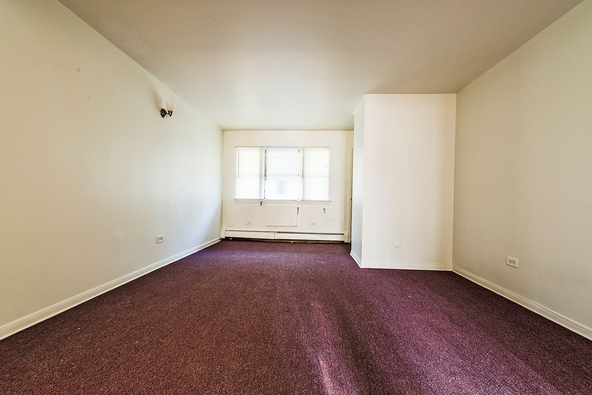 Empty room with burgundy carpet, white walls, and a window.