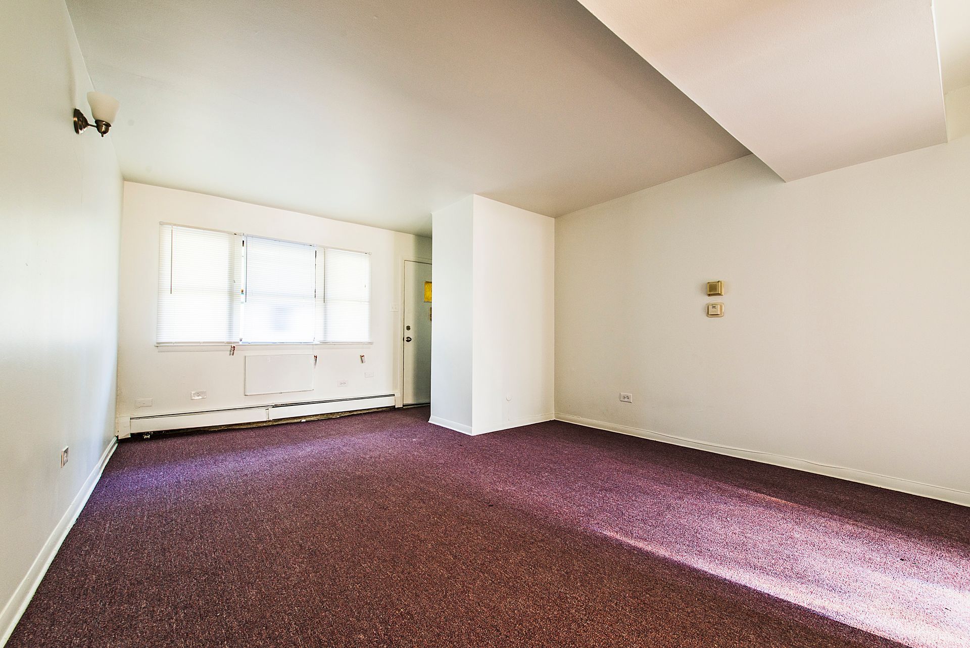 Empty room with purple carpet, white walls, and a window.