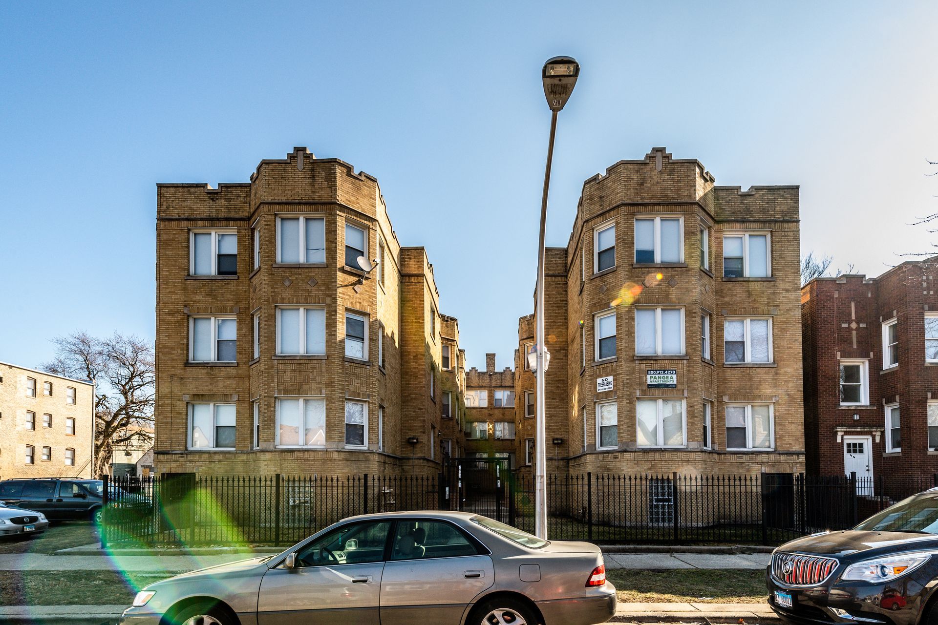 Two tan brick apartment buildings with decorative tops, street, cars, and a streetlight.