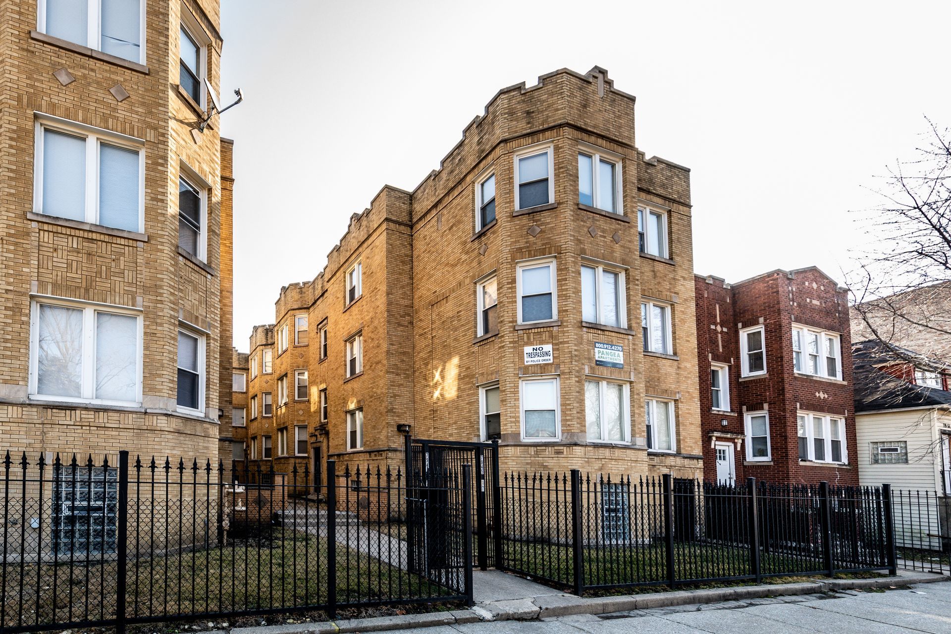 Brick apartment buildings with black iron fences in an urban setting.