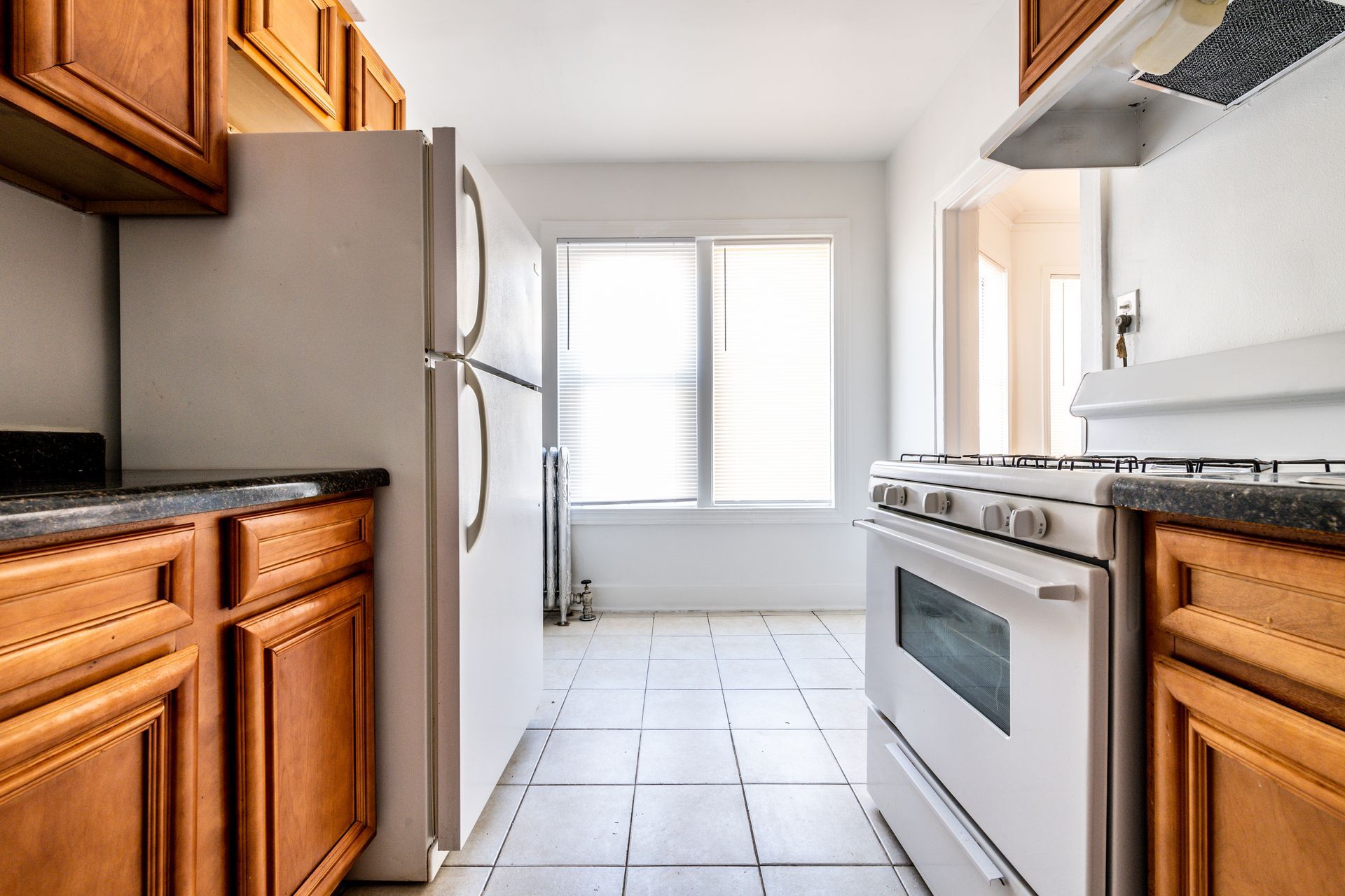 Kitchen with wooden cabinets, white appliances, window, and tiled floor.