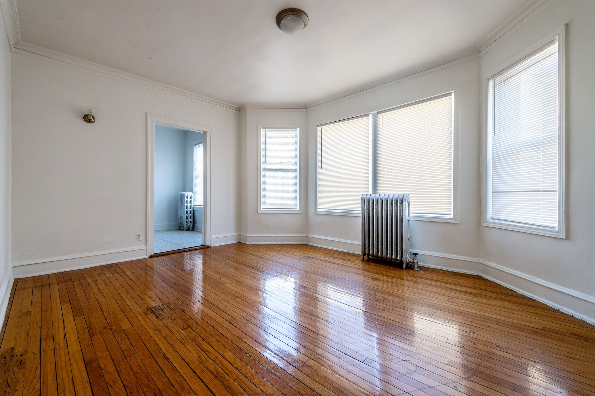 Empty room with hardwood floors, white walls, and large windows.