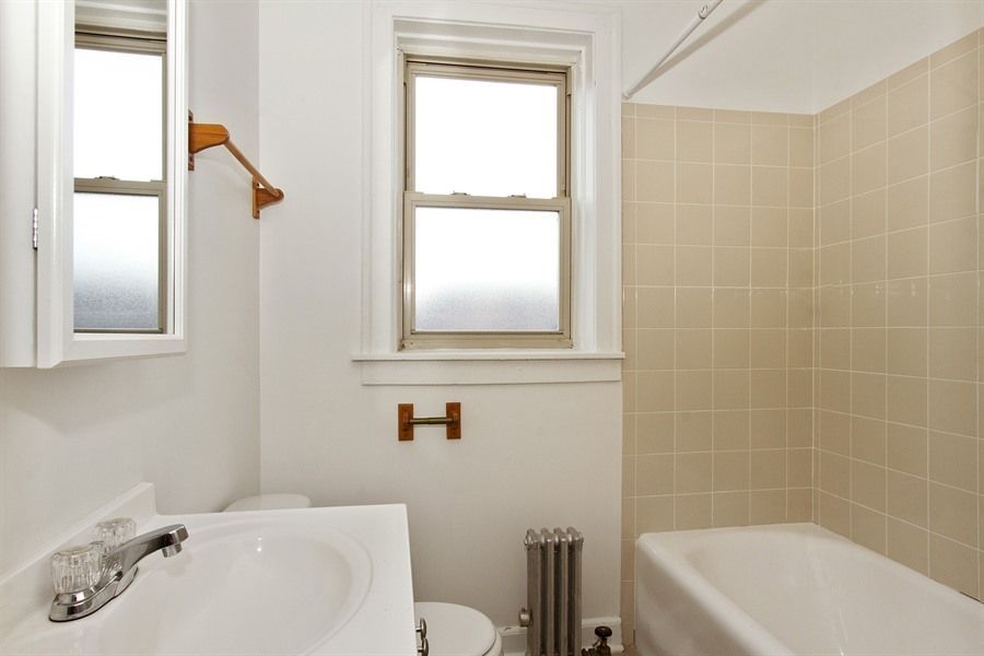 Bathroom with a white sink, toilet, tub, and beige tiled walls; a window lets in light.