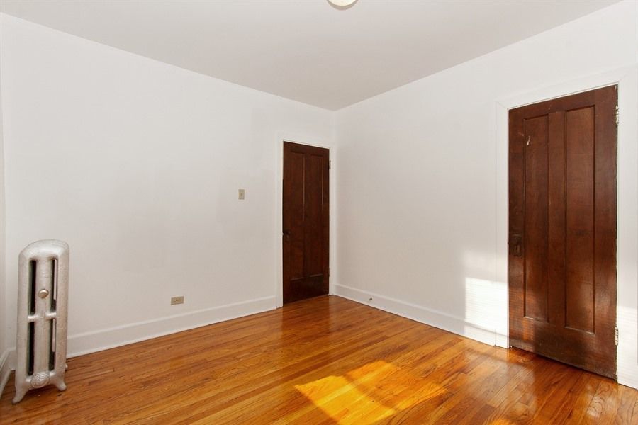 Empty room with hardwood floors, white walls, two brown doors, and a radiator.
